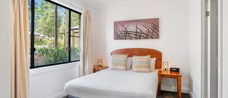 A bedroom with a bed, a ceiling fan, a window with curtains, a nightstand, and a wall-mounted artwork.