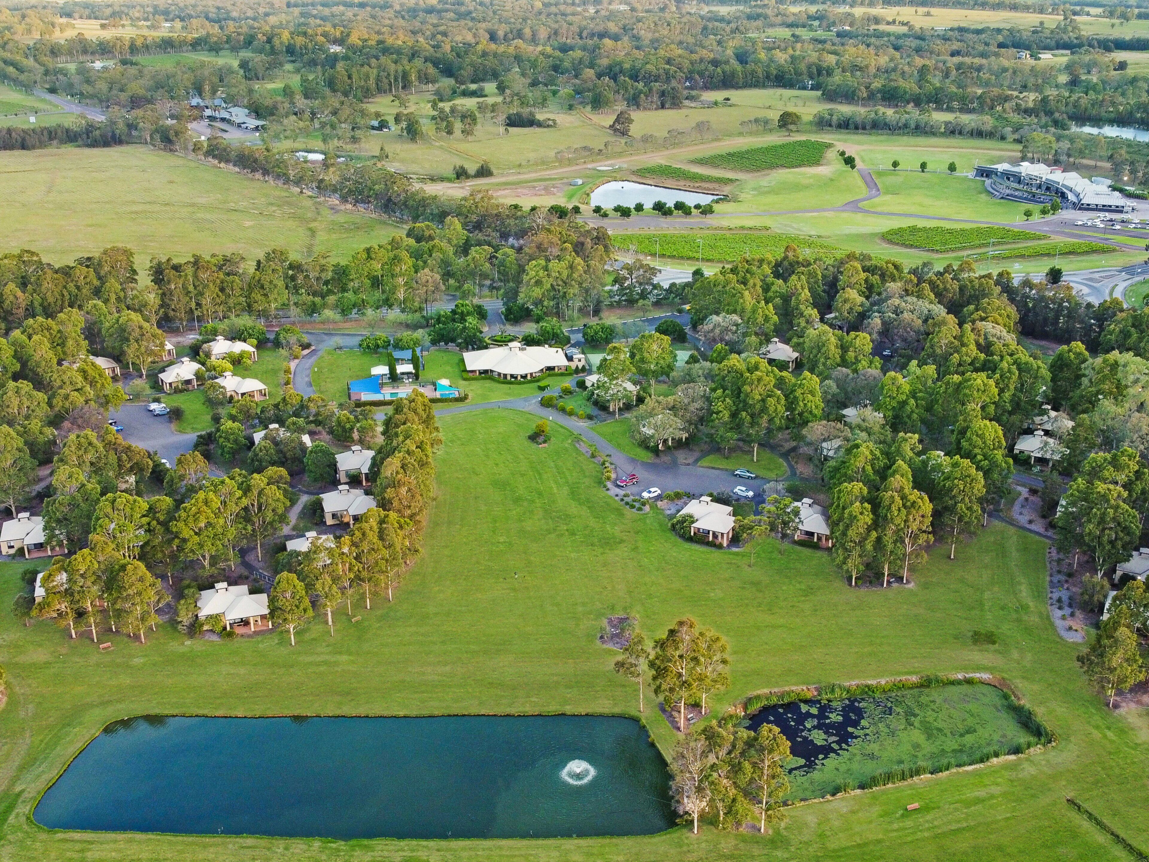 An aerial view of a golf course with multiple buildings, a pond, and surrounding greenery.