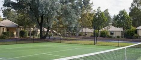 Una cancha de tenis con una red, rodeada de árboles y casas.
