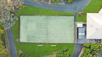 Eine Vogelperspektive auf einen Tennisplatz, umgeben von Grünflächen und Wohnhäusern.