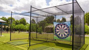 A fenced area with a dartboard mounted on a wall, surrounded by artificial turf.
