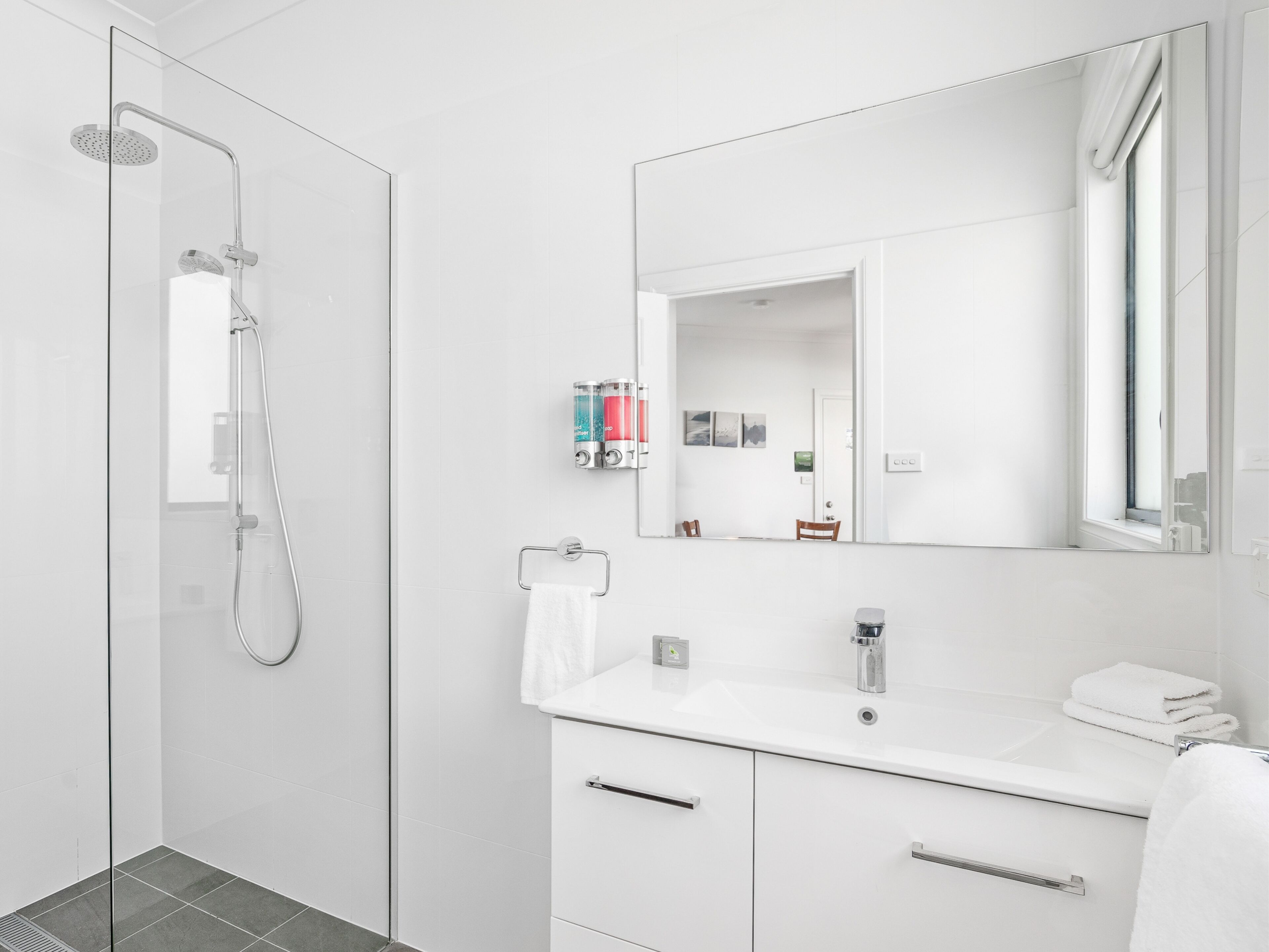 Ein modernes Badezimmer mit Duschkabine aus Glas, einem weißen Waschbecken mit Spiegel darüber und einem kleinen Schrank darunter.