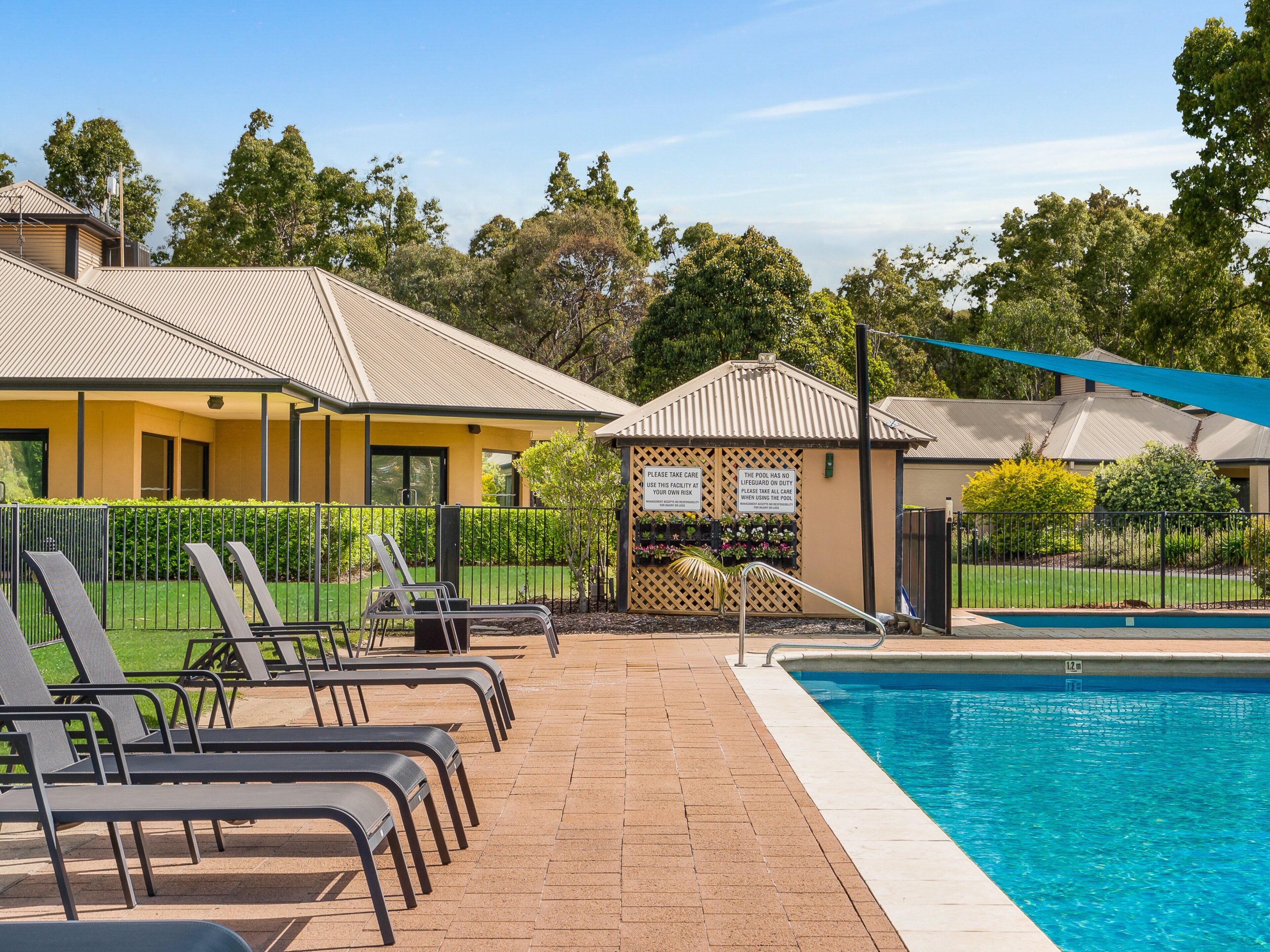 A pool area with lounge chairs, a pool, and a building with a sign warning about pool safety.