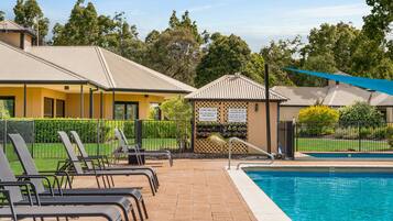 A pool area with lounge chairs, a pool, and a building with a sign warning about pool safety.