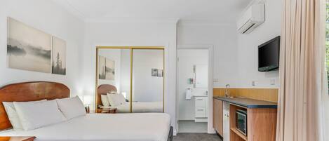 A hotel room with a bed, bedside table, mirror, TV, and a kitchenette.