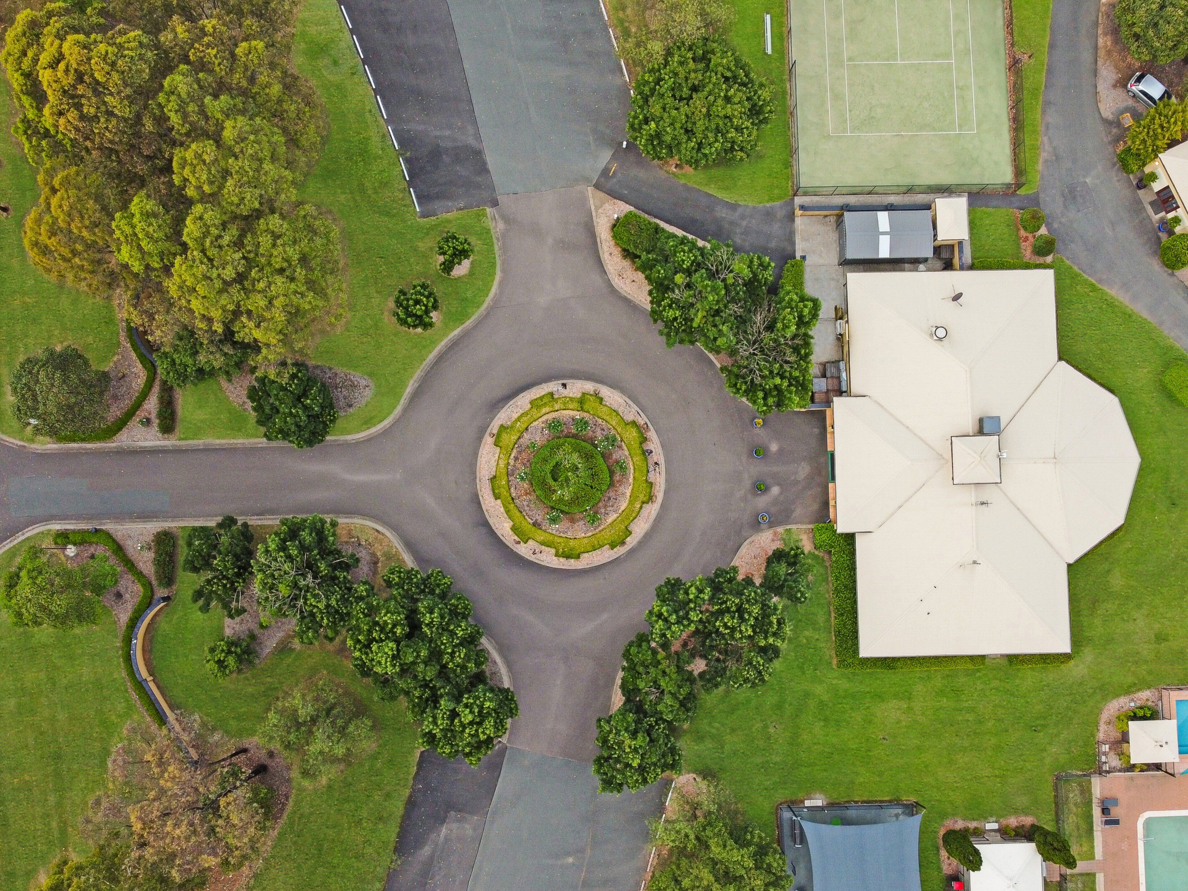 An aerial view of a roundabout with surrounding greenery and a building with a large white roof.