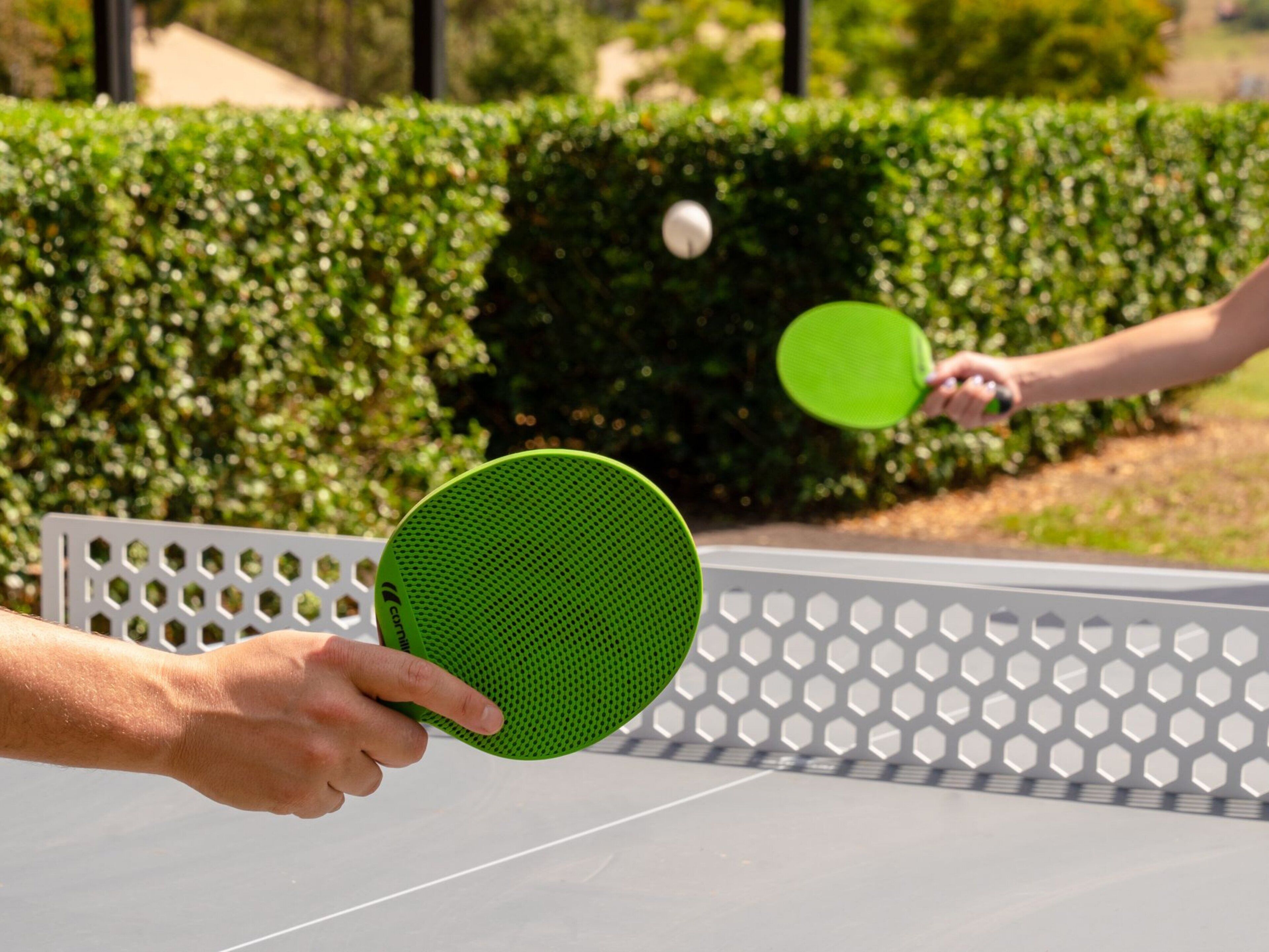 Two people playing table tennis on an outdoor table.