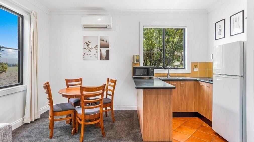 A compact kitchen with a dining area, featuring a wooden table and chairs, a small island counter, and a refrigerator.