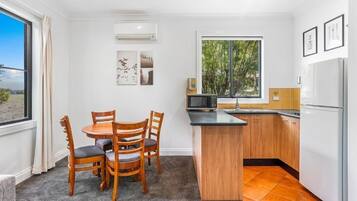 A compact kitchen with a dining area, featuring a wooden table and chairs, a small island counter, and a refrigerator.