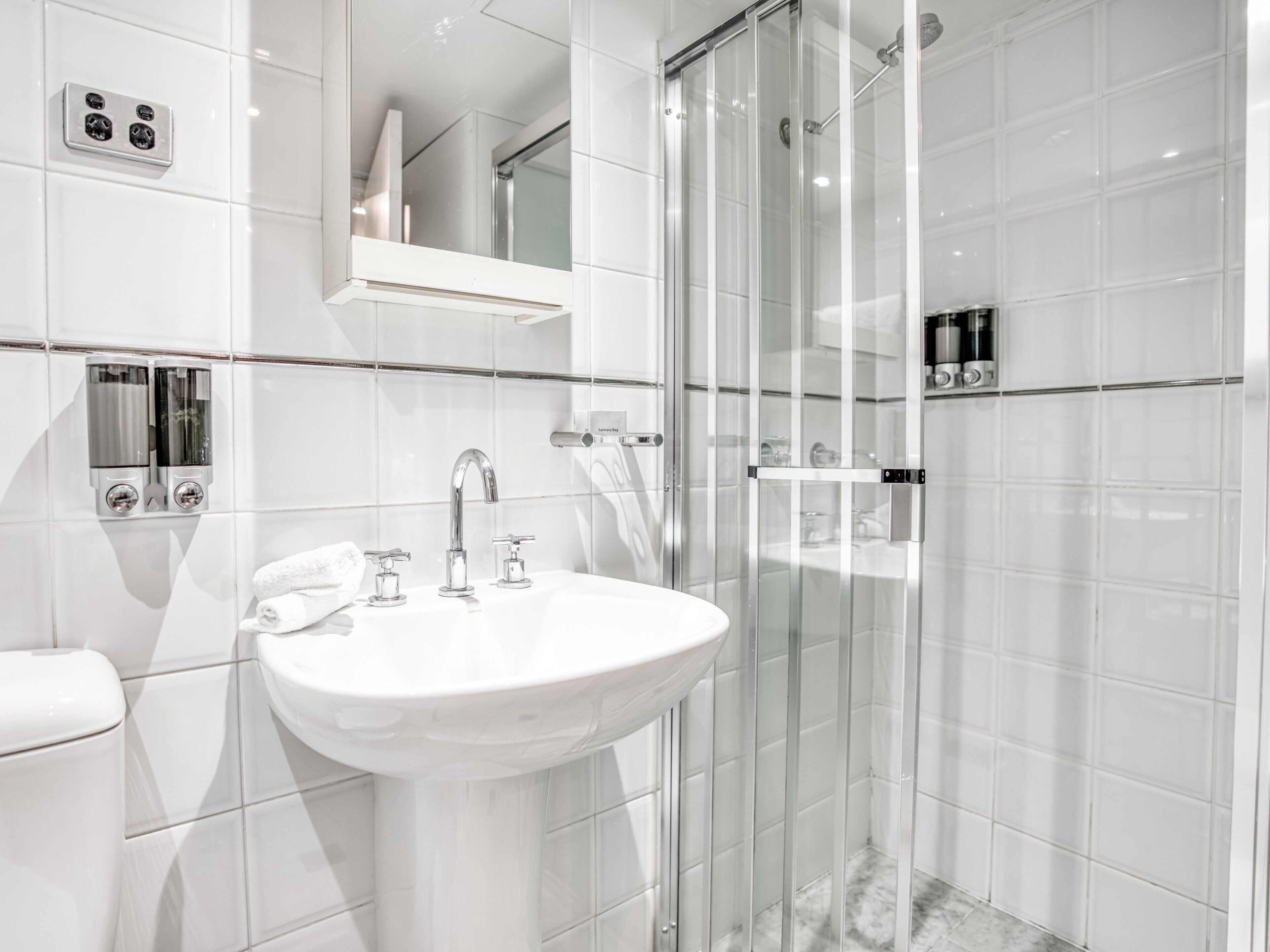 A modern bathroom with a white sink, a glass shower enclosure, and a mirror above the sink.