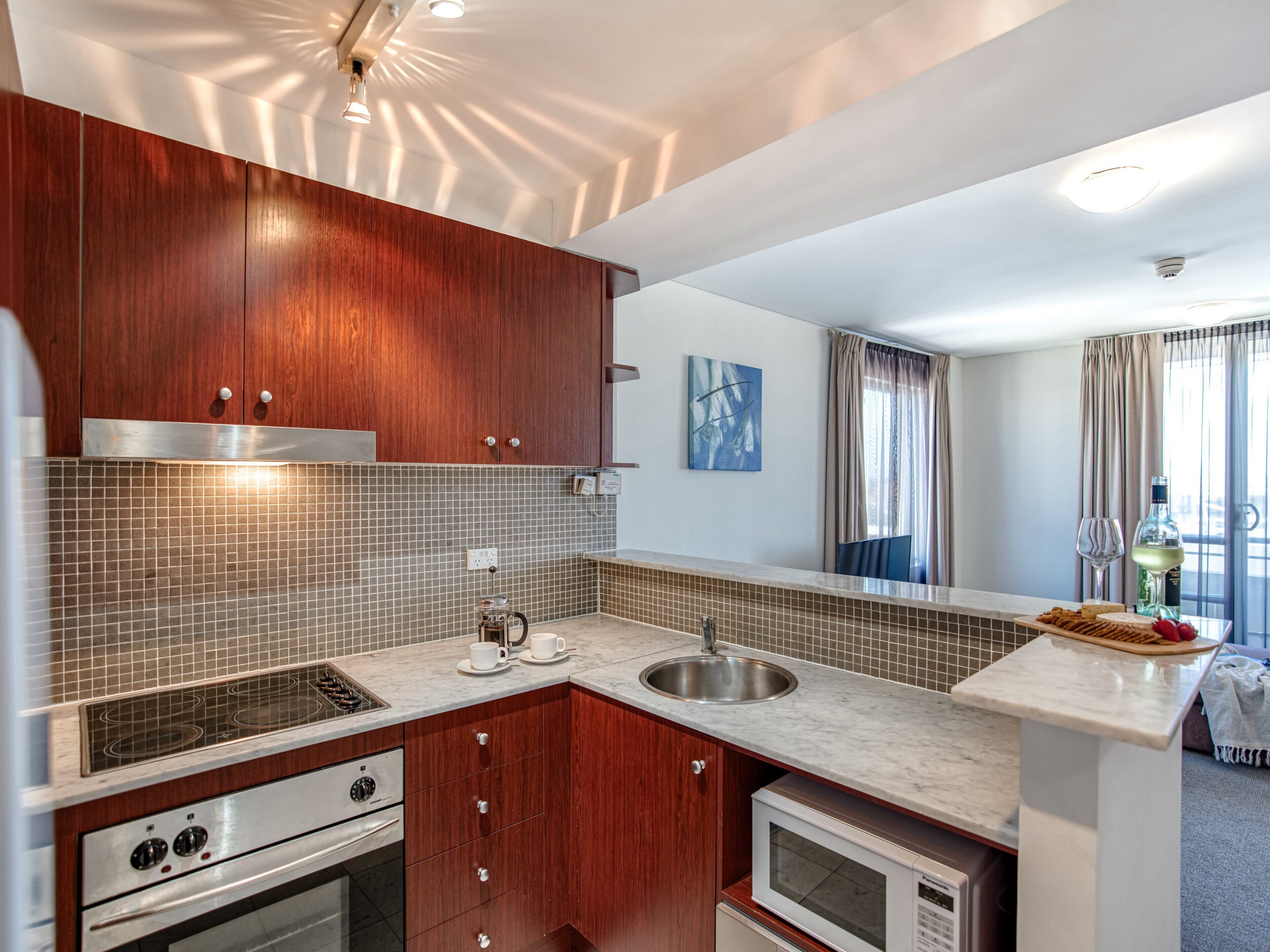 A modern kitchen with wooden cabinets, a tiled backsplash, a built-in oven, a microwave, and a sink.