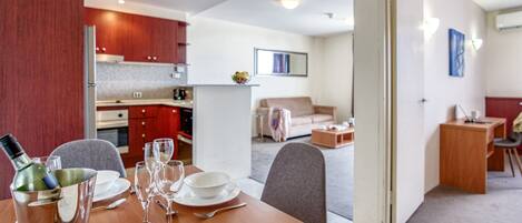 A modern kitchen with wooden cabinets, a dining table set with plates, glasses, and cutlery, and a living area with a sofa and a coffee table.