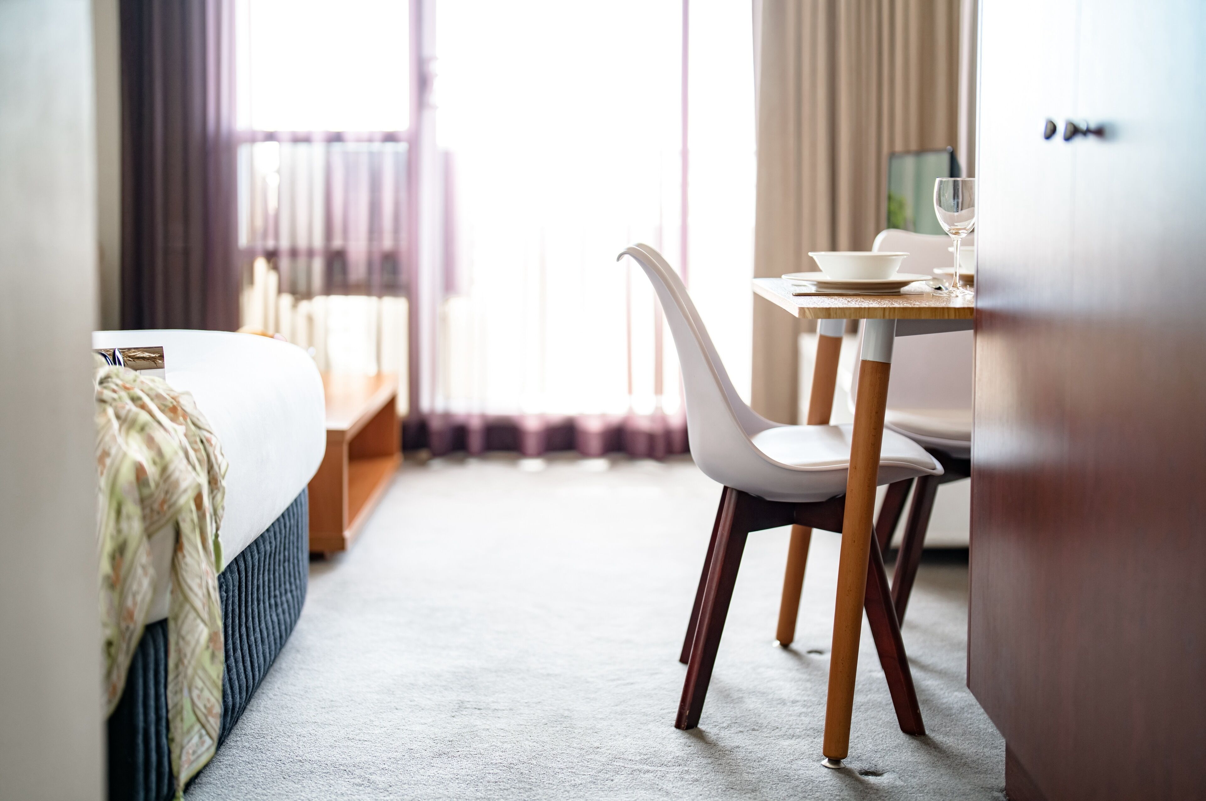 A hotel room with a bed, a dining table with chairs, and a wardrobe.