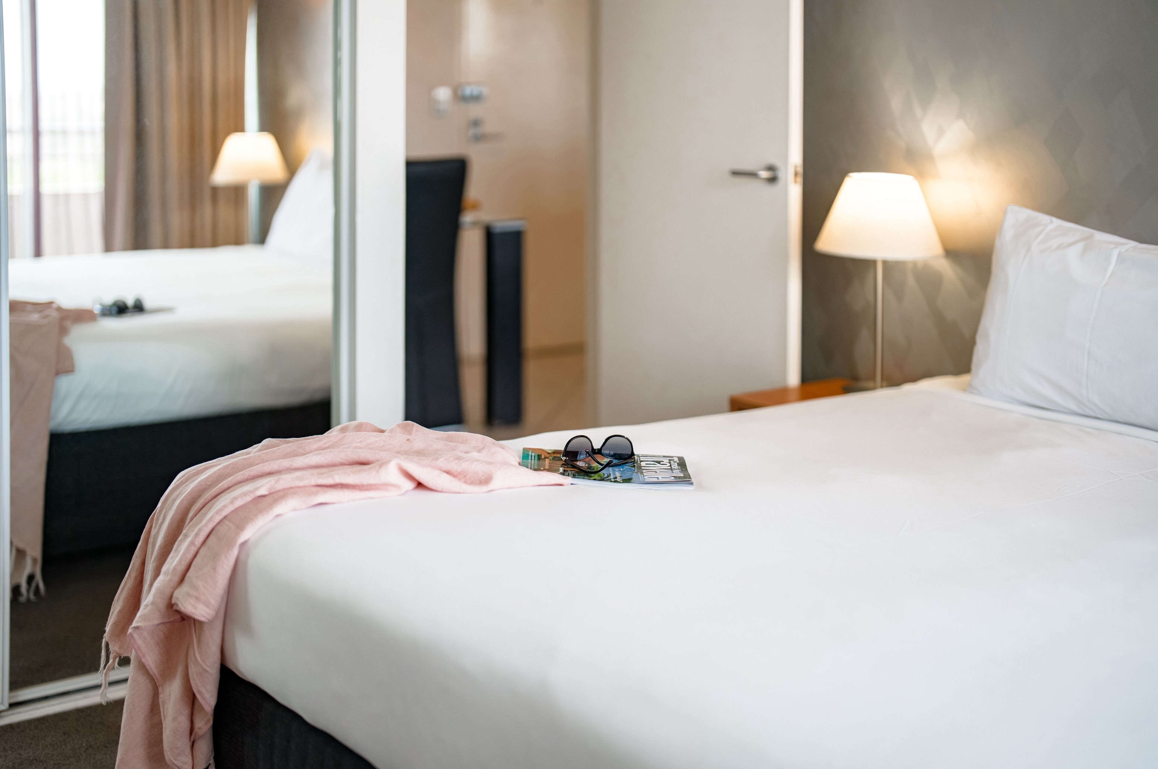 Una habitación de hotel con una cama, una mesita de noche, una lámpara y un espejo.