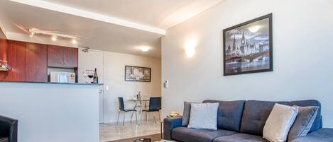 Ein modernes Wohnzimmer mit einem grauen Sofa, einem Glastisch und einem Essbereich mit Tisch und Stühlen.