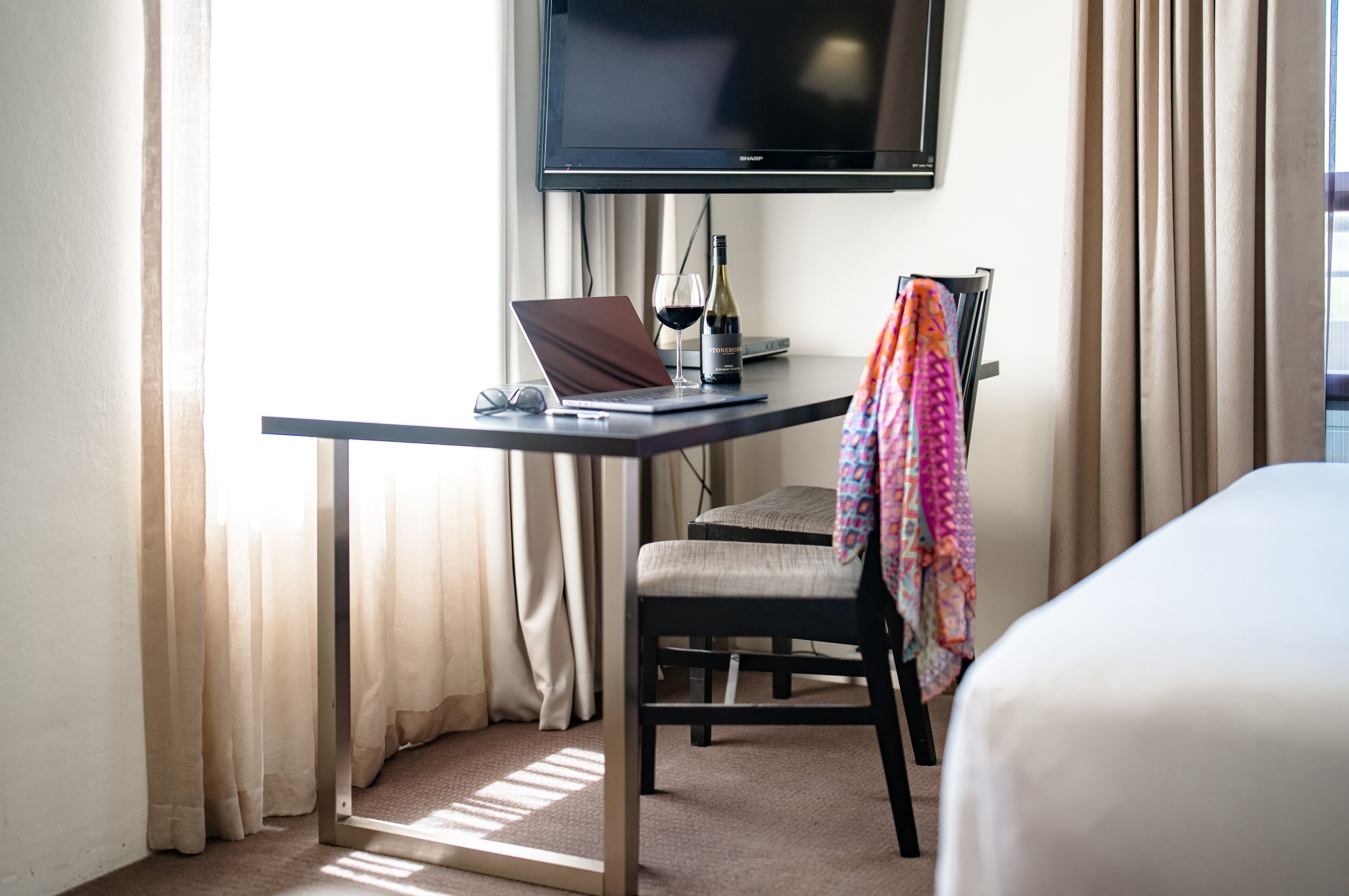 A hotel room with a desk, laptop, wine bottle, and glasses.