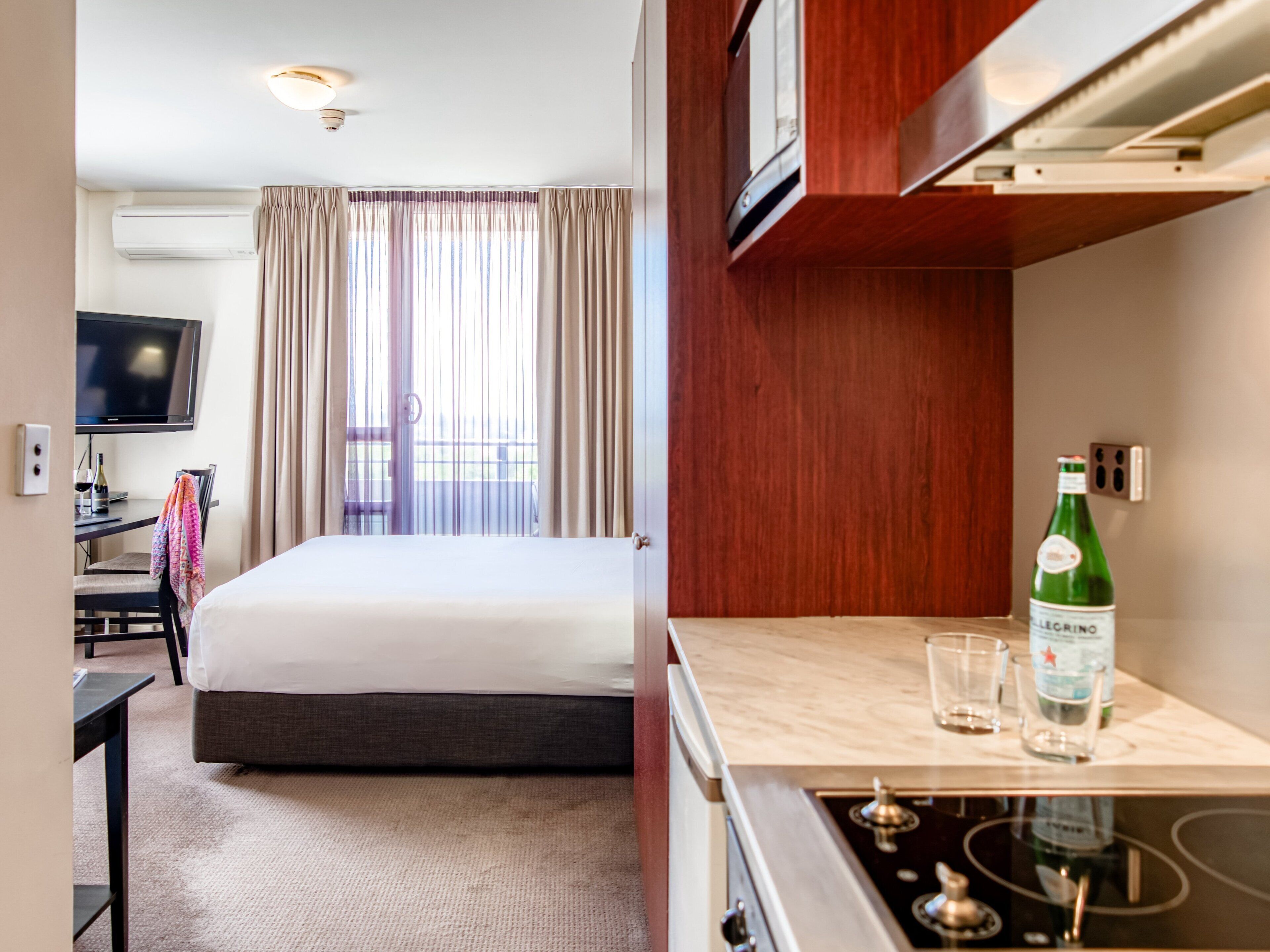 A hotel room with a bed, a desk with a chair, a television, and a window with curtains.