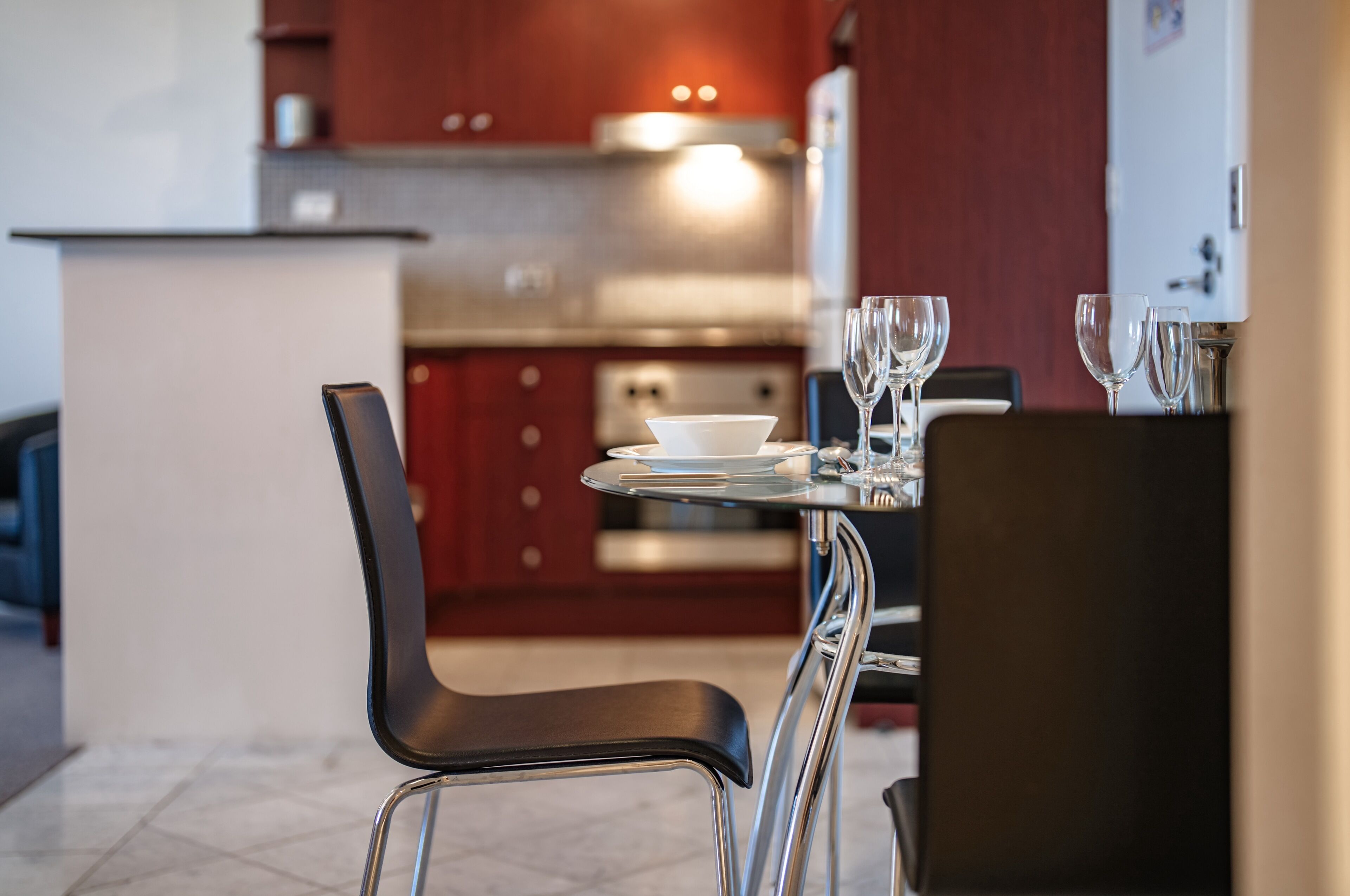 Une cuisine moderne avec un coin repas, comprenant une table dressée avec un saladier et des verres à vin, ainsi qu’une chaise avec un siège noir.