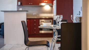 Une cuisine moderne avec un coin repas, comprenant une table dressée avec un saladier et des verres à vin, ainsi qu’une chaise avec un siège noir.