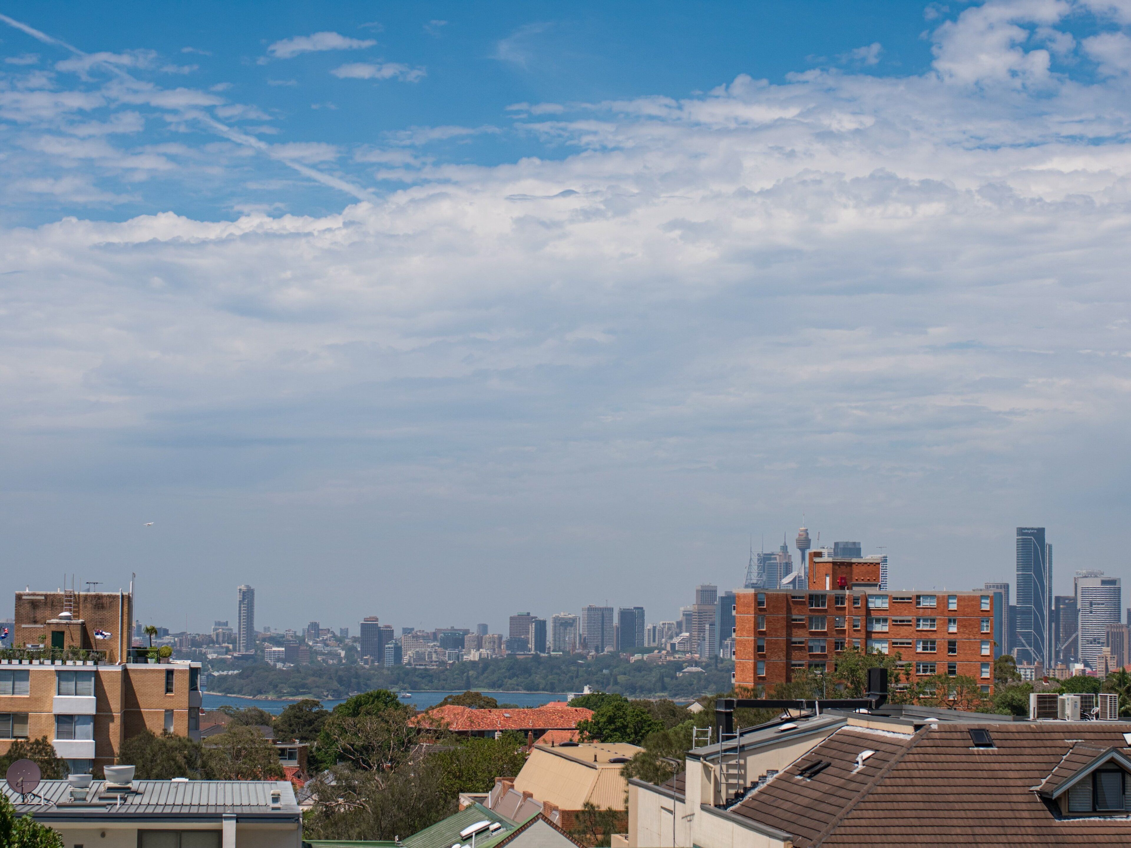 A cityscape with modern buildings, a clear sky, and a distant view of a body of water.