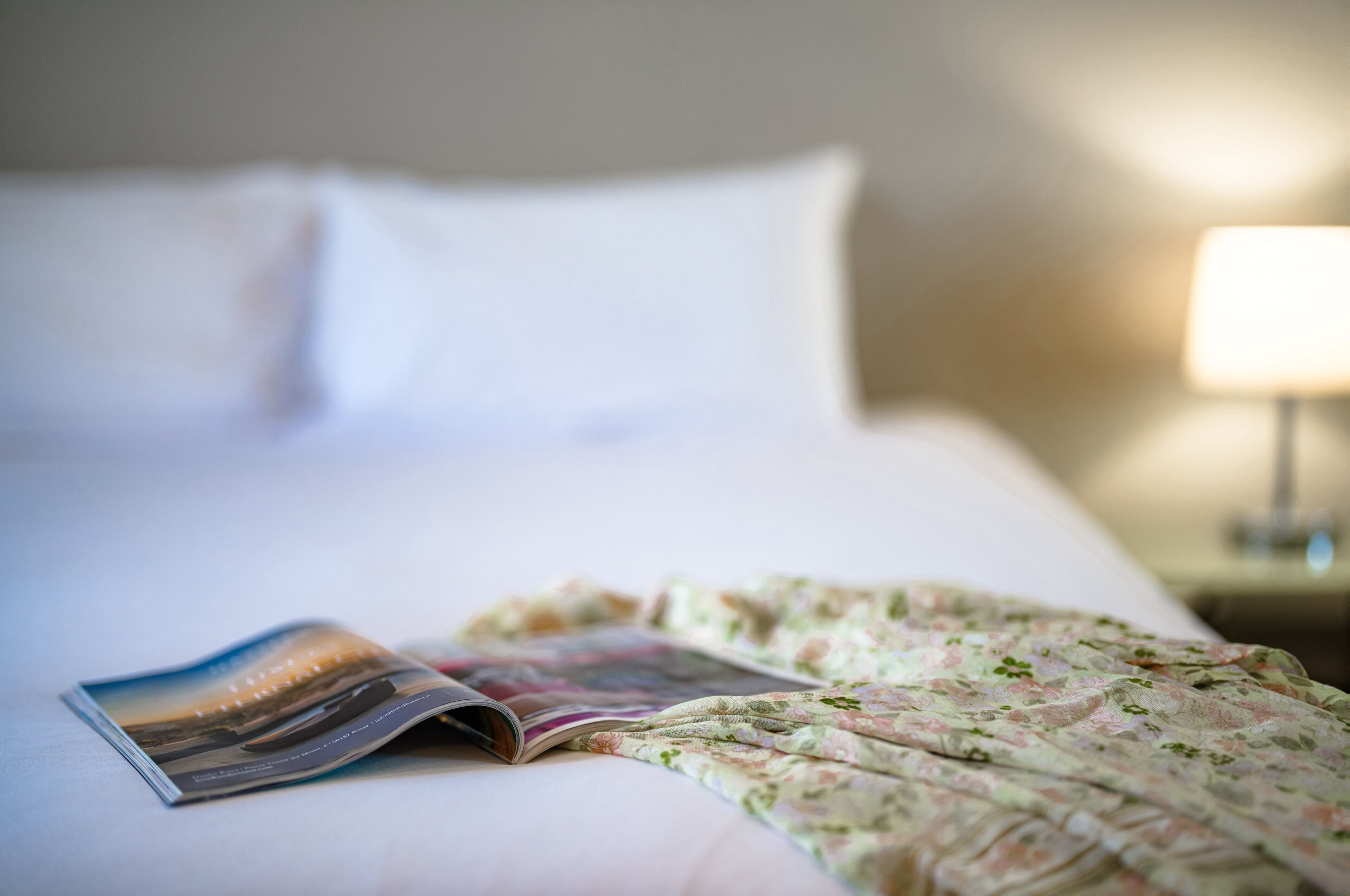 A neatly made bed with a floral blanket and a magazine on it.