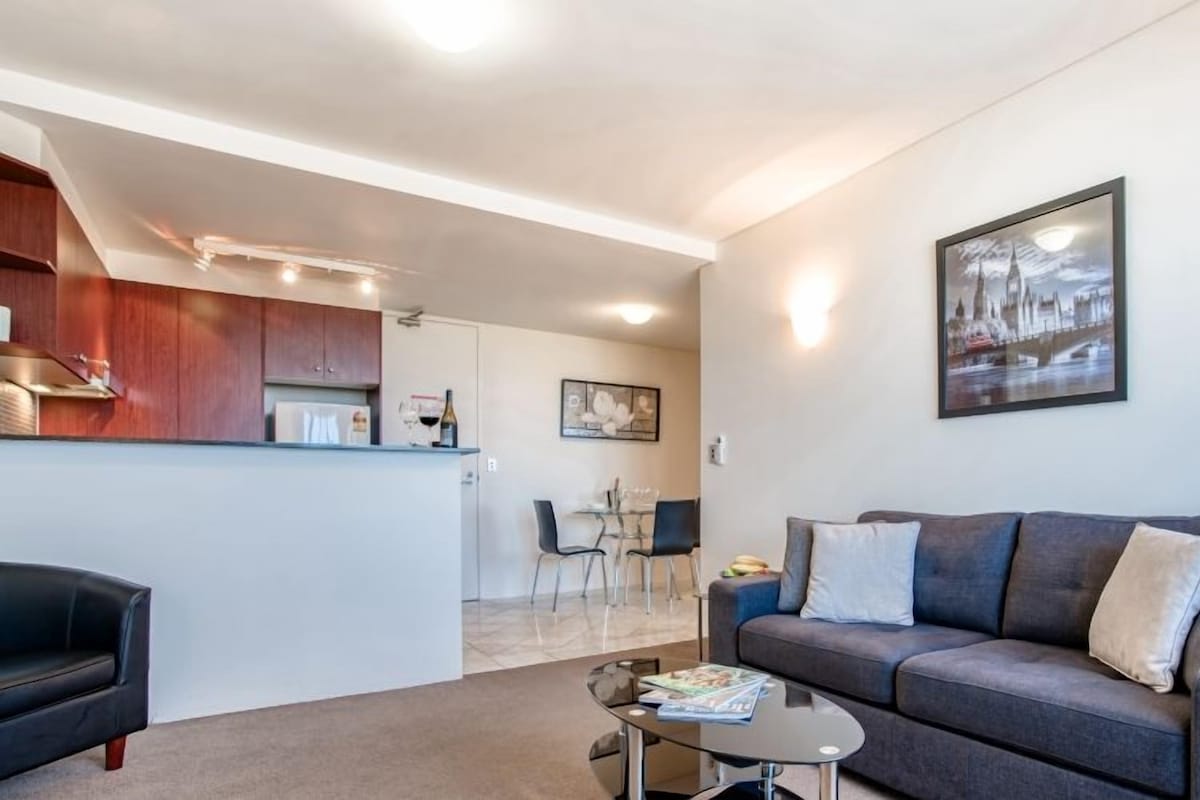 A modern living room with a grey sofa, a coffee table, and a dining area with chairs and a table.