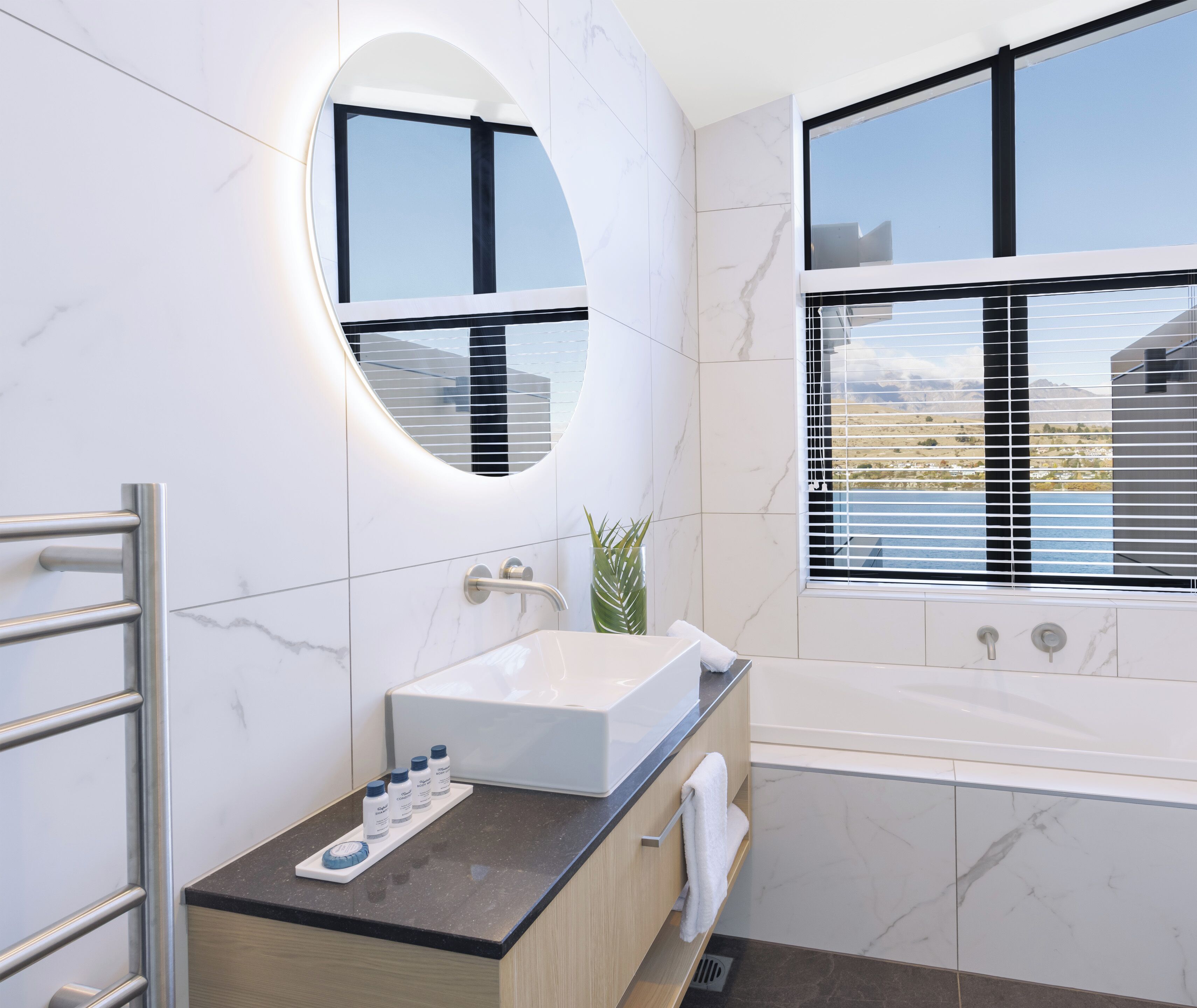 A modern bathroom with a large oval mirror, a built-in sink, and a bathtub.