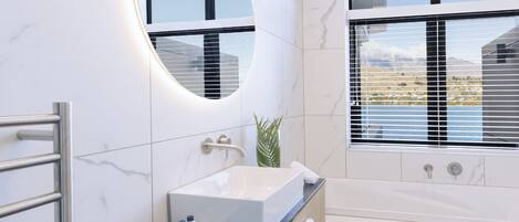 A modern bathroom with a large oval mirror, a built-in sink, and a bathtub.