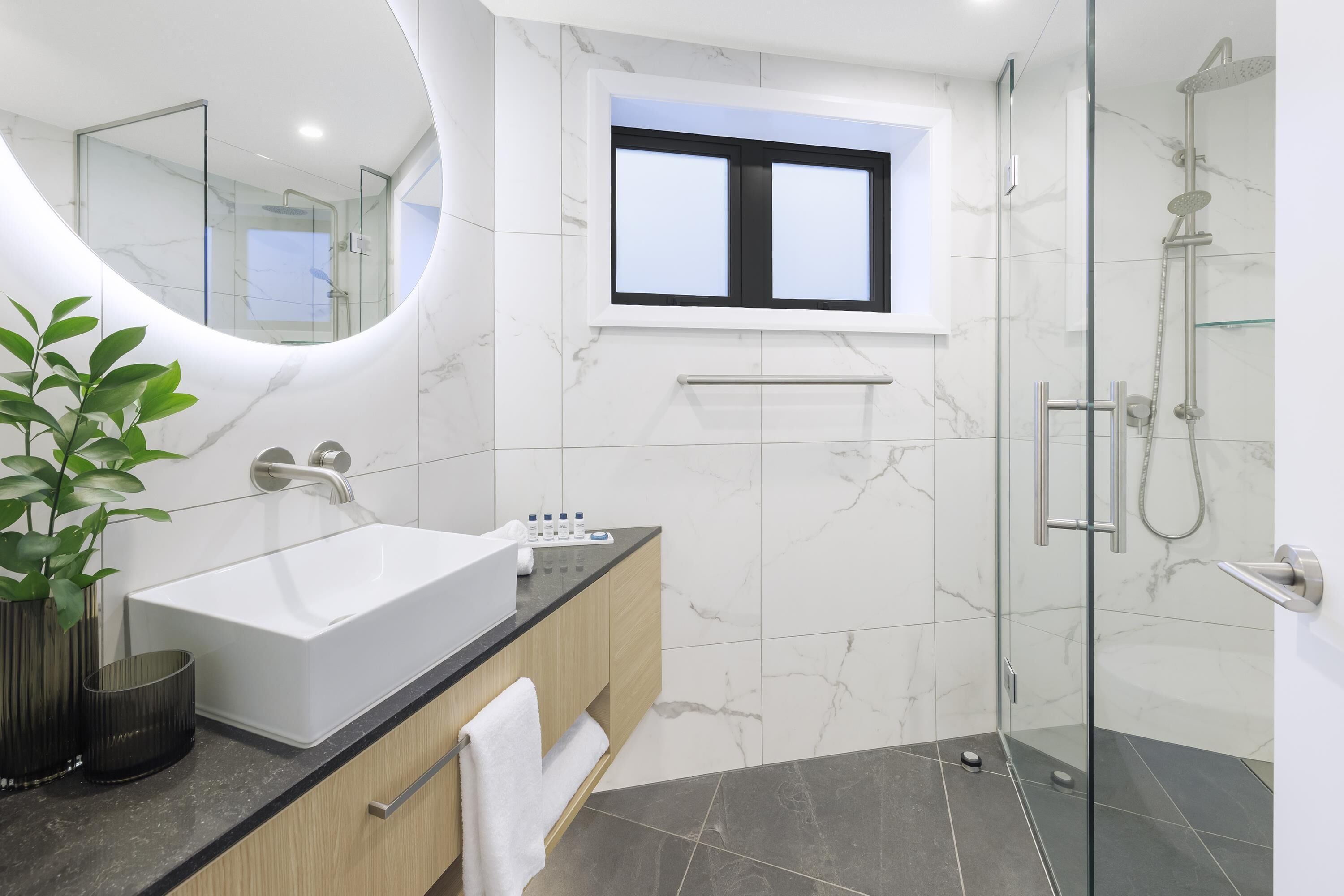 A modern bathroom with a large white sink, a glass shower enclosure, and a marble-tiled wall.