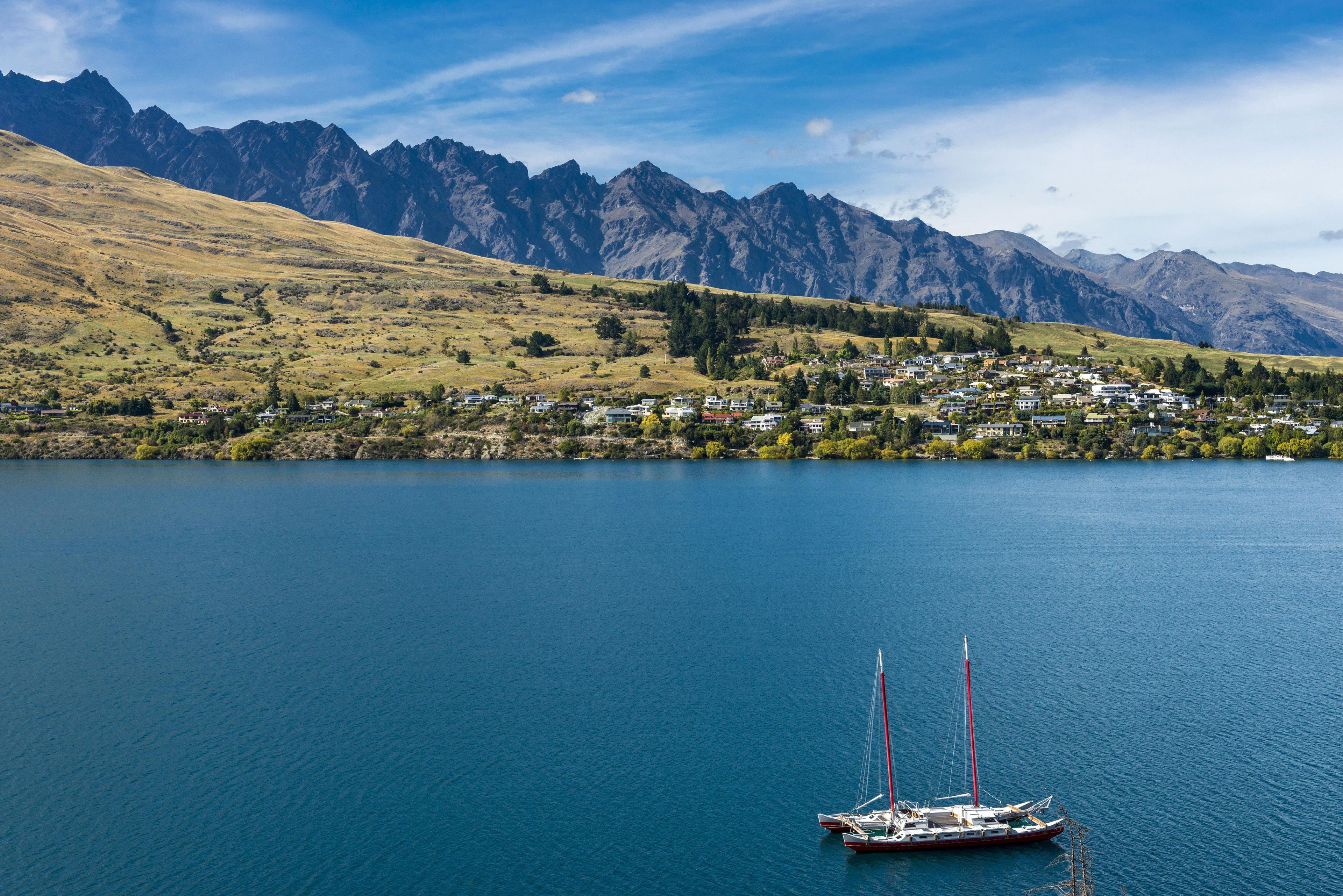 A lake with a sailboat, surrounded by mountains and a small town.