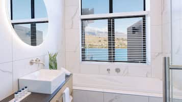 Un baño moderno con un espejo ovalado grande, una bañera independiente y un ventanal con persianas.