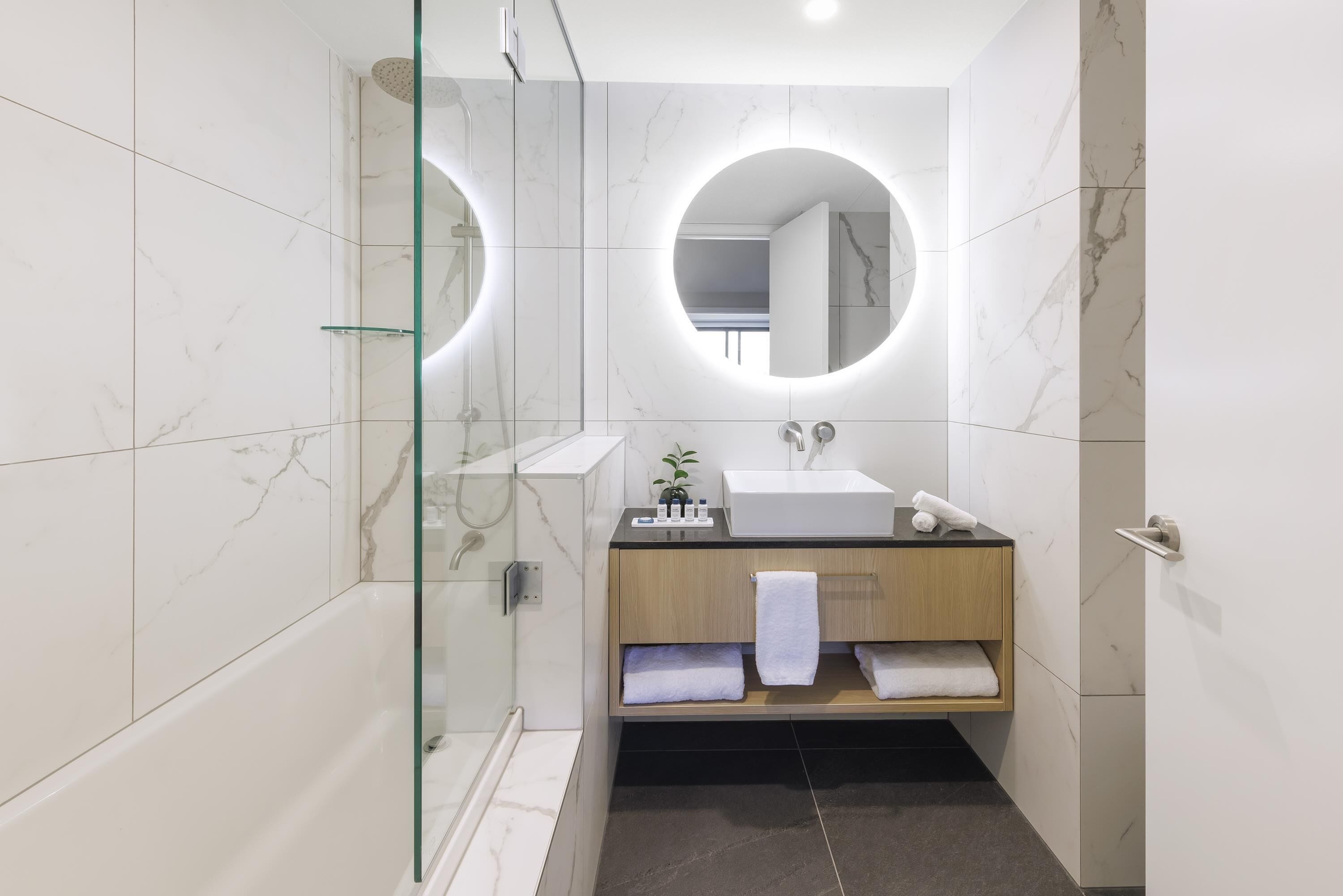 A modern bathroom with a glass-enclosed shower, a wooden vanity with a sink, and two round mirrors.
