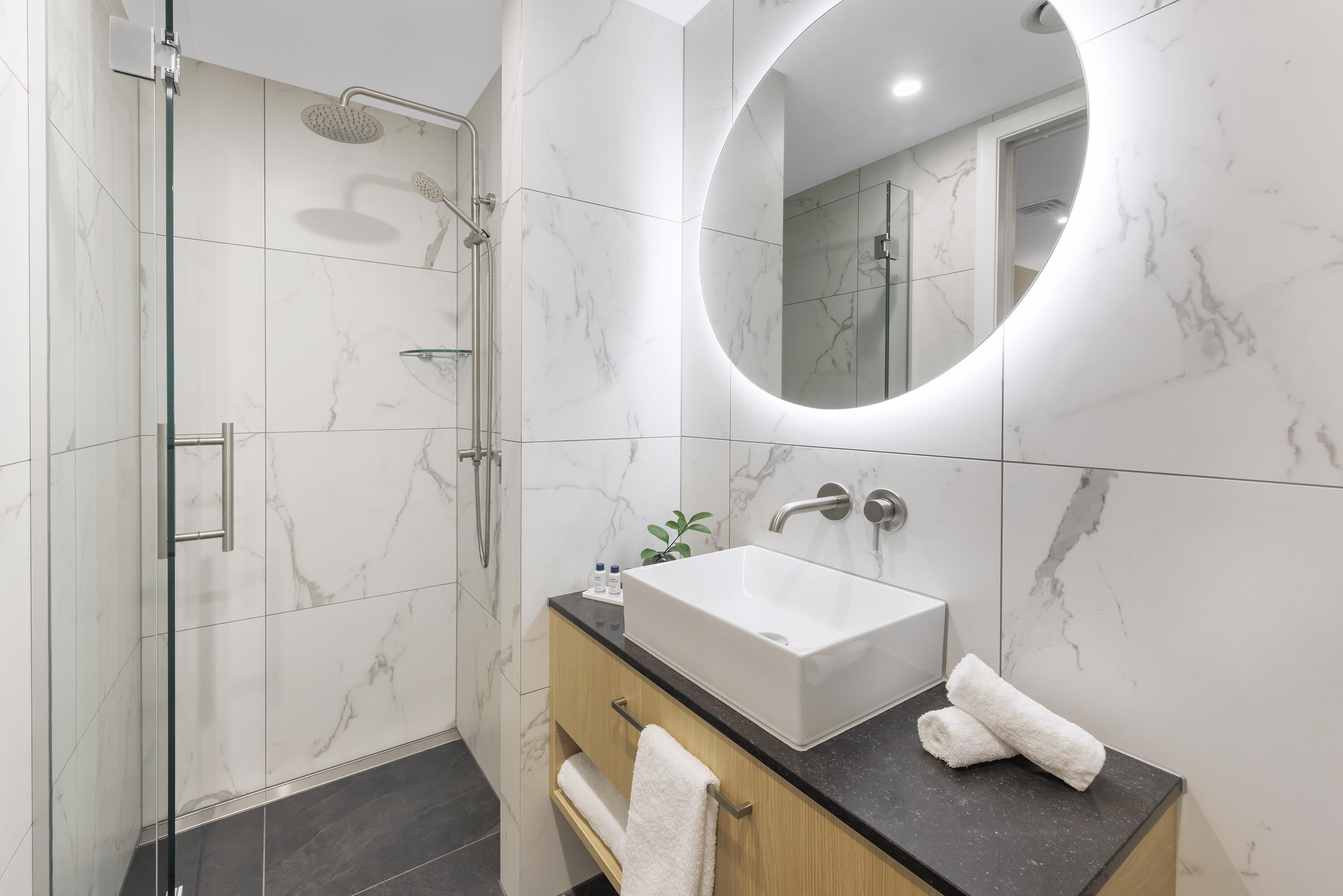 A modern bathroom with a glass-enclosed shower, a large mirror, and a sink with a marble countertop.