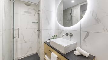 A modern bathroom with a glass-enclosed shower, a large mirror, and a sink with a marble countertop.