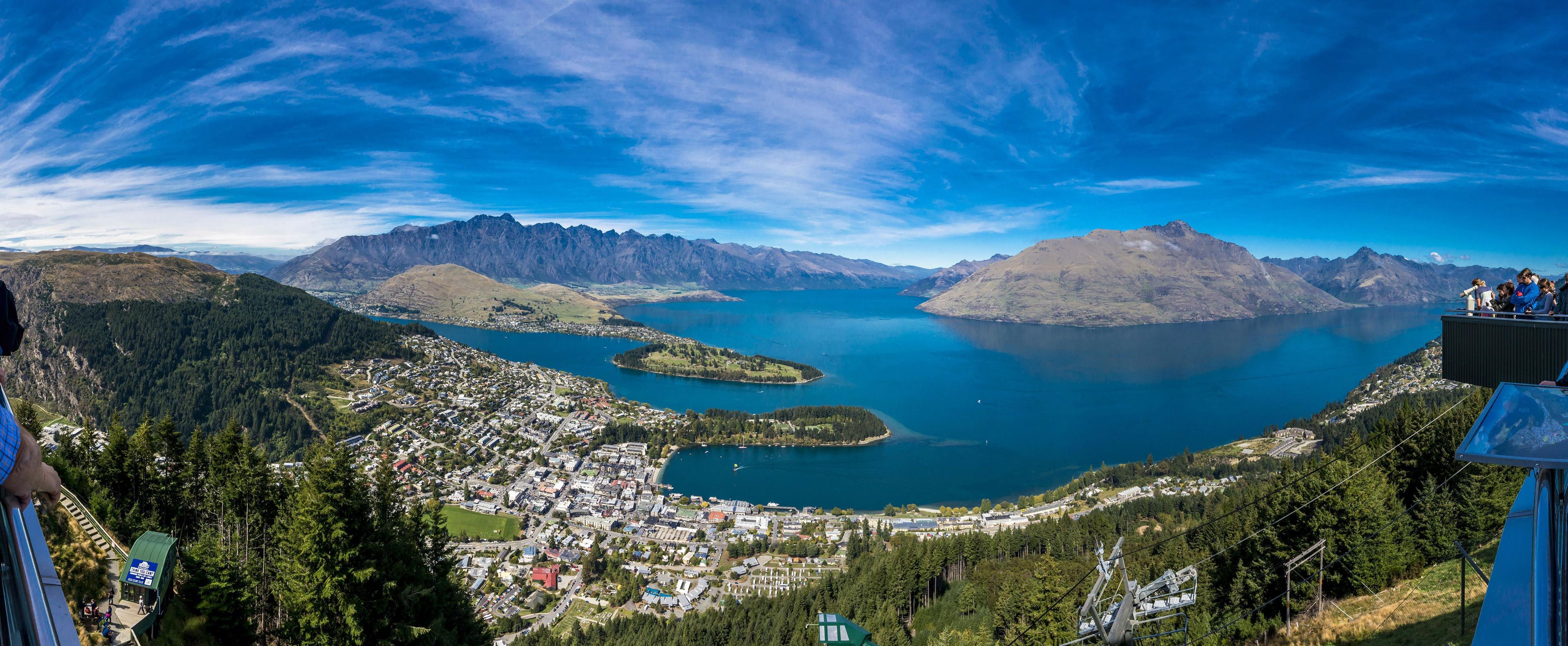 A panoramic view of a town with a lake, mountains, and a clear sky.