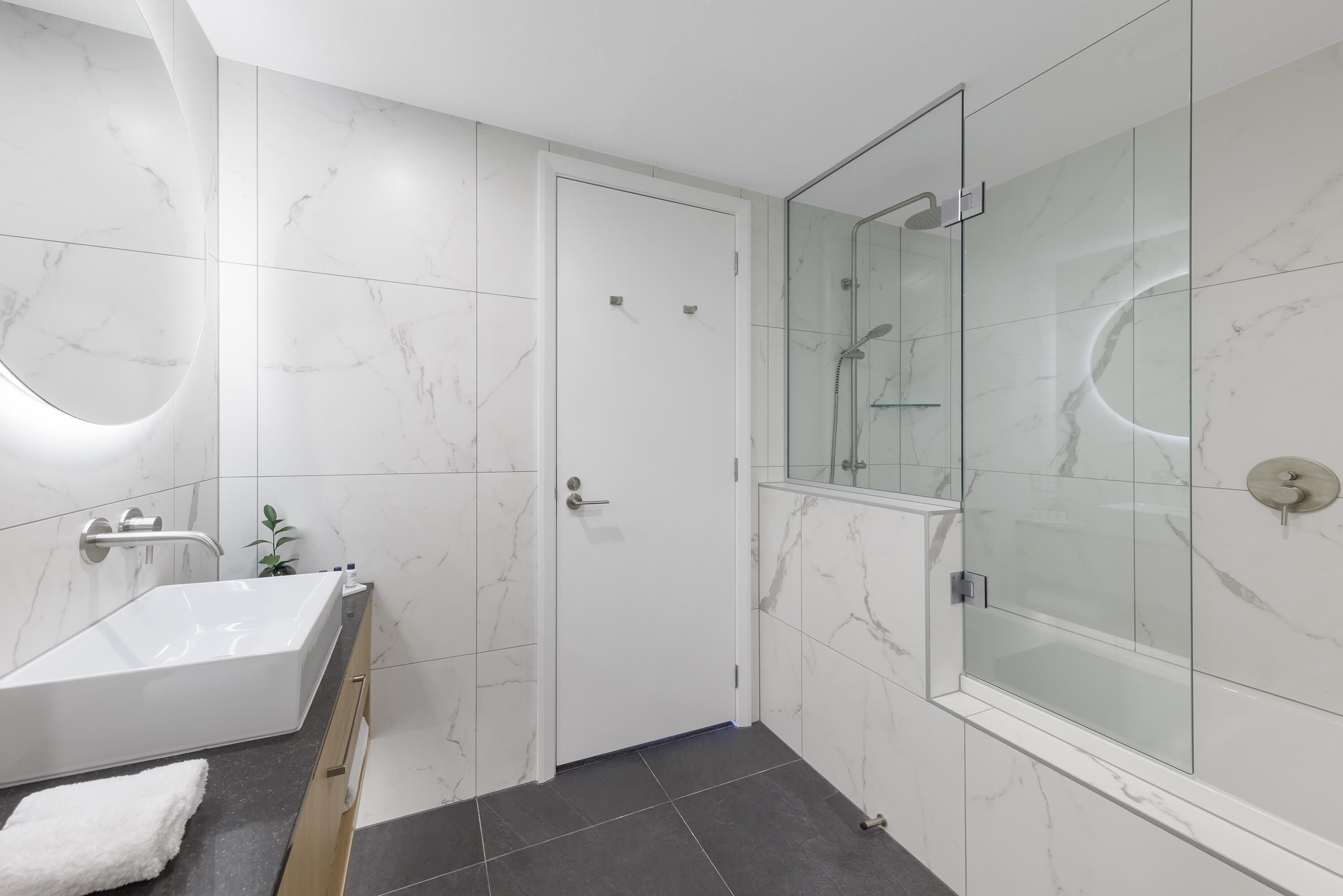 Ein modernes Badezimmer mit einer freistehenden Badewanne, einer einteiligen Duschkabine und Marmorwänden.