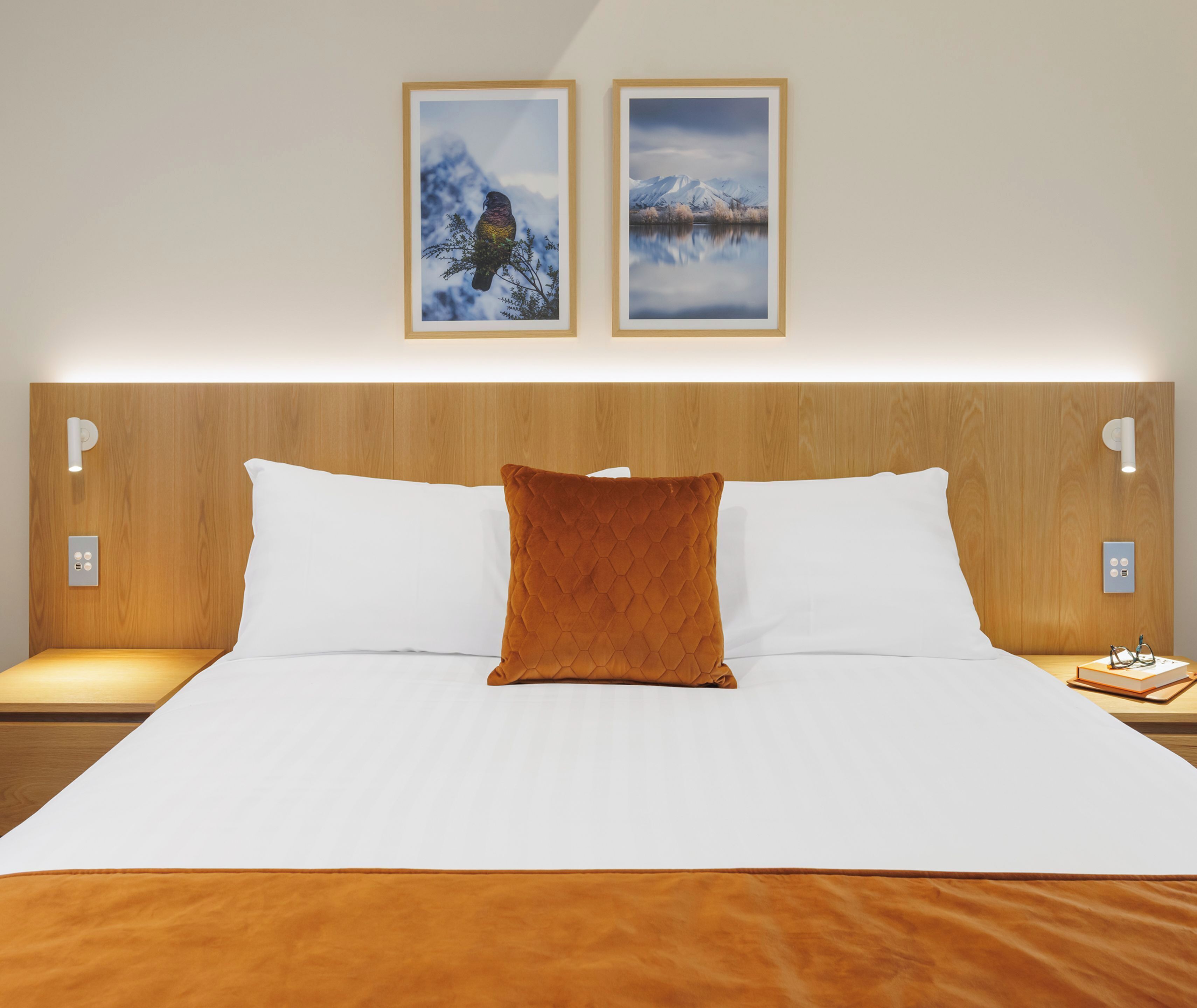 A hotel room with a large bed, two wall-mounted light fixtures, and two framed pictures above the bed.