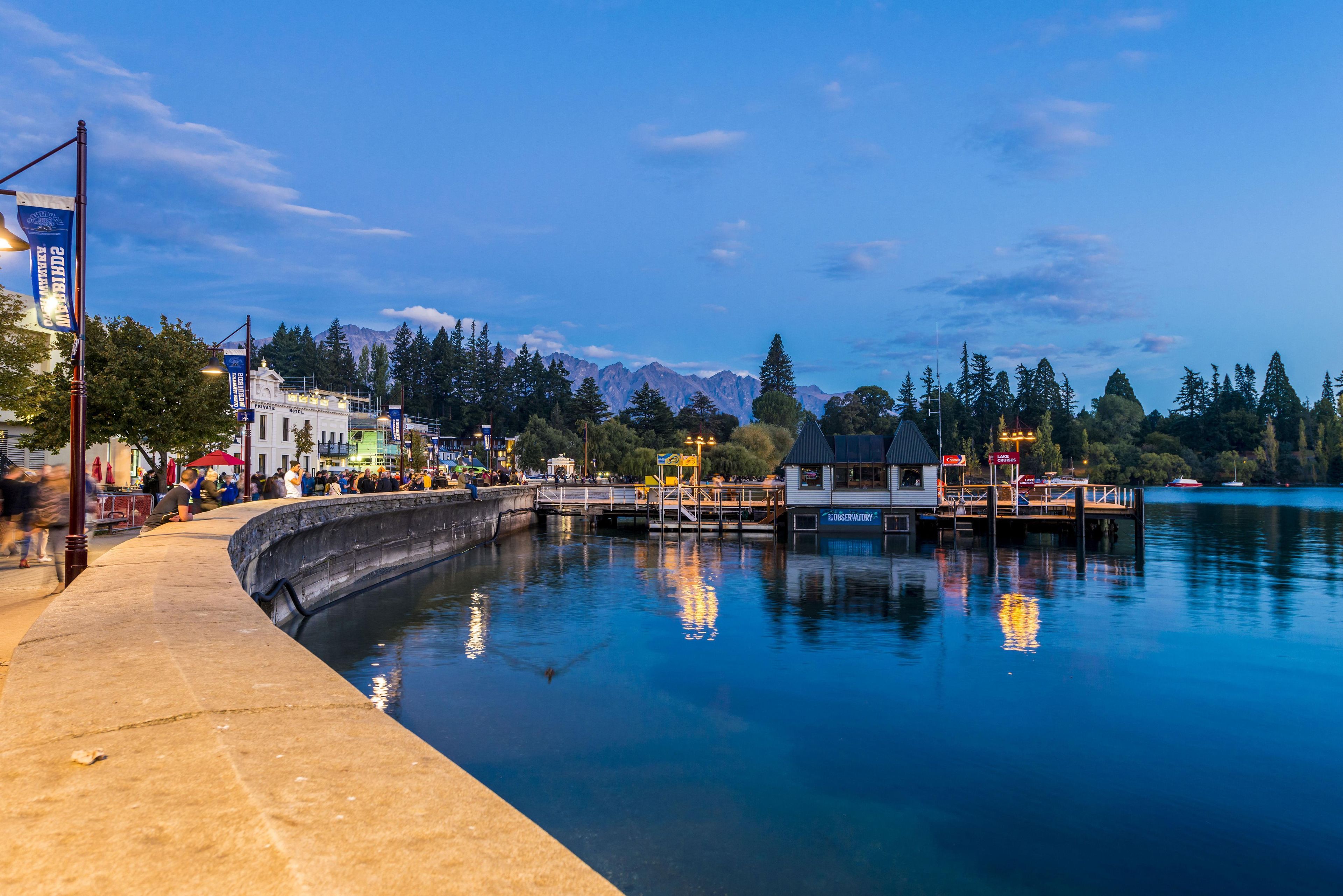 A waterfront hotel with a dock, a bridge, and a mountain backdrop.
