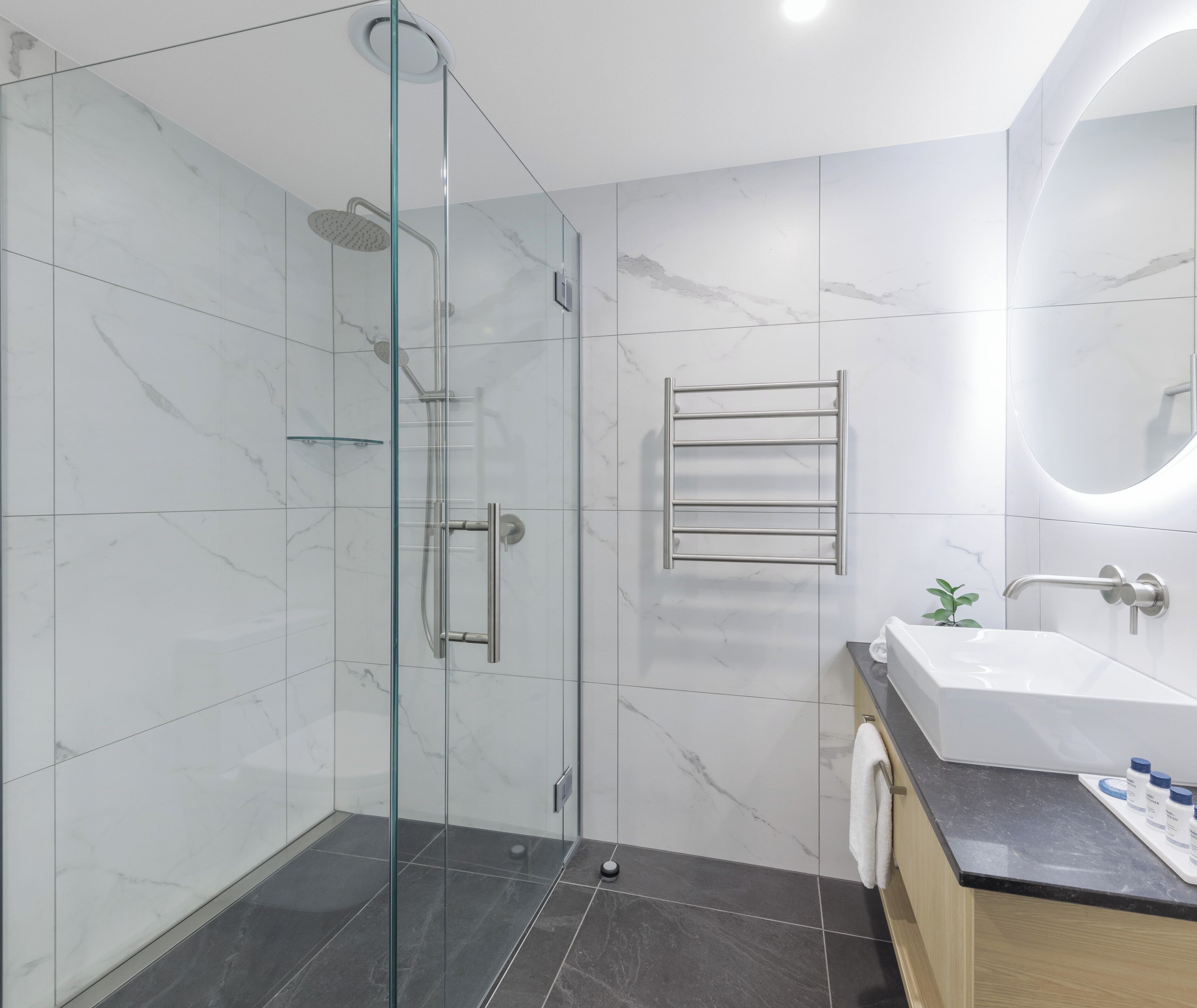 Een moderne badkamer met een douchecabine van glas, een wastafel met spiegel en een handdoekrek.