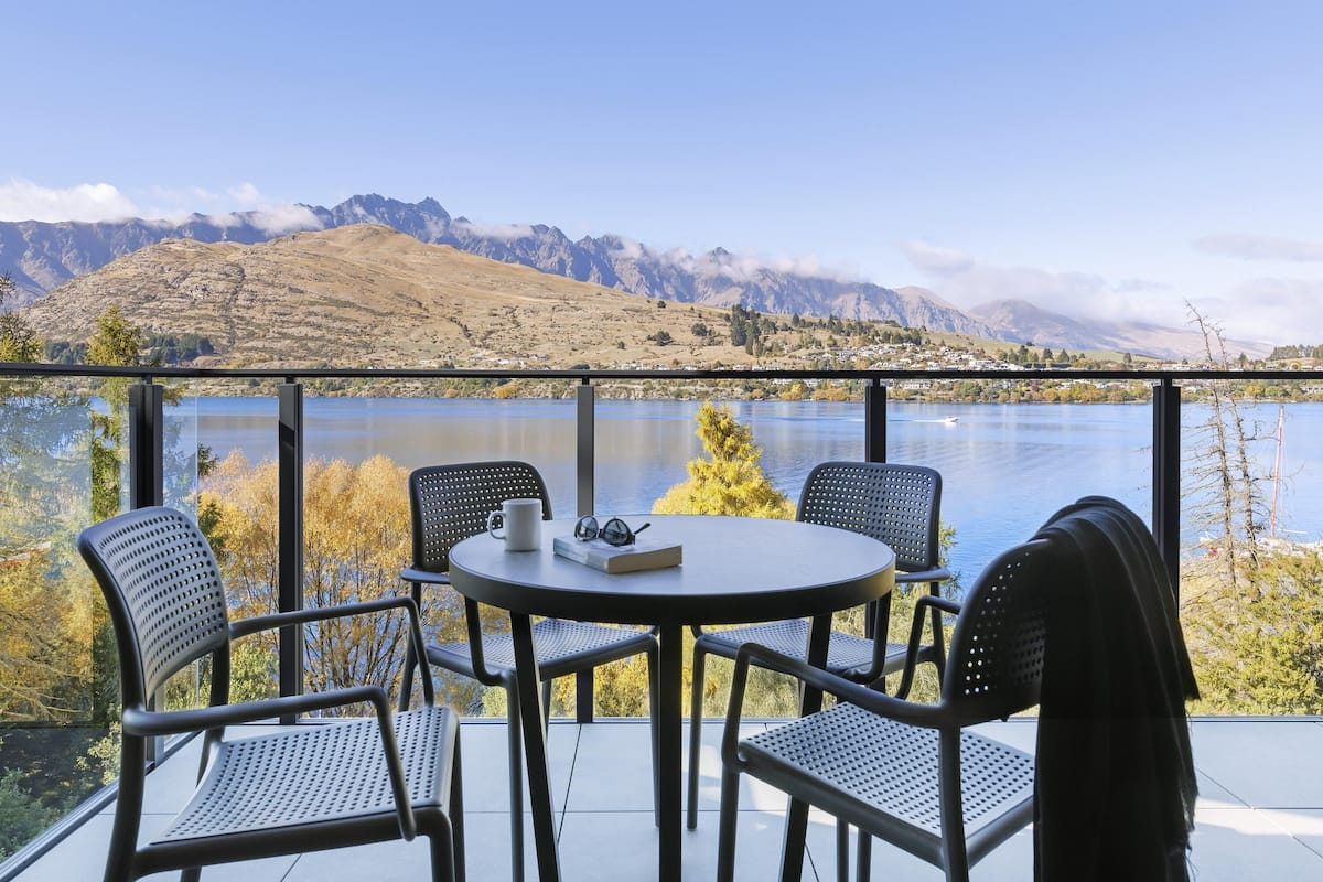 Un balcón con una mesa redonda y cuatro sillas, con vistas a un lago y montañas.