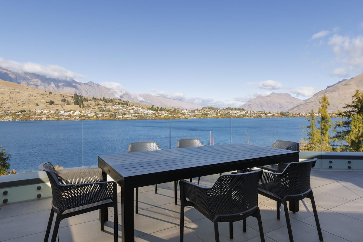 Una terraza con una mesa y sillas que da a un lago y montañas.