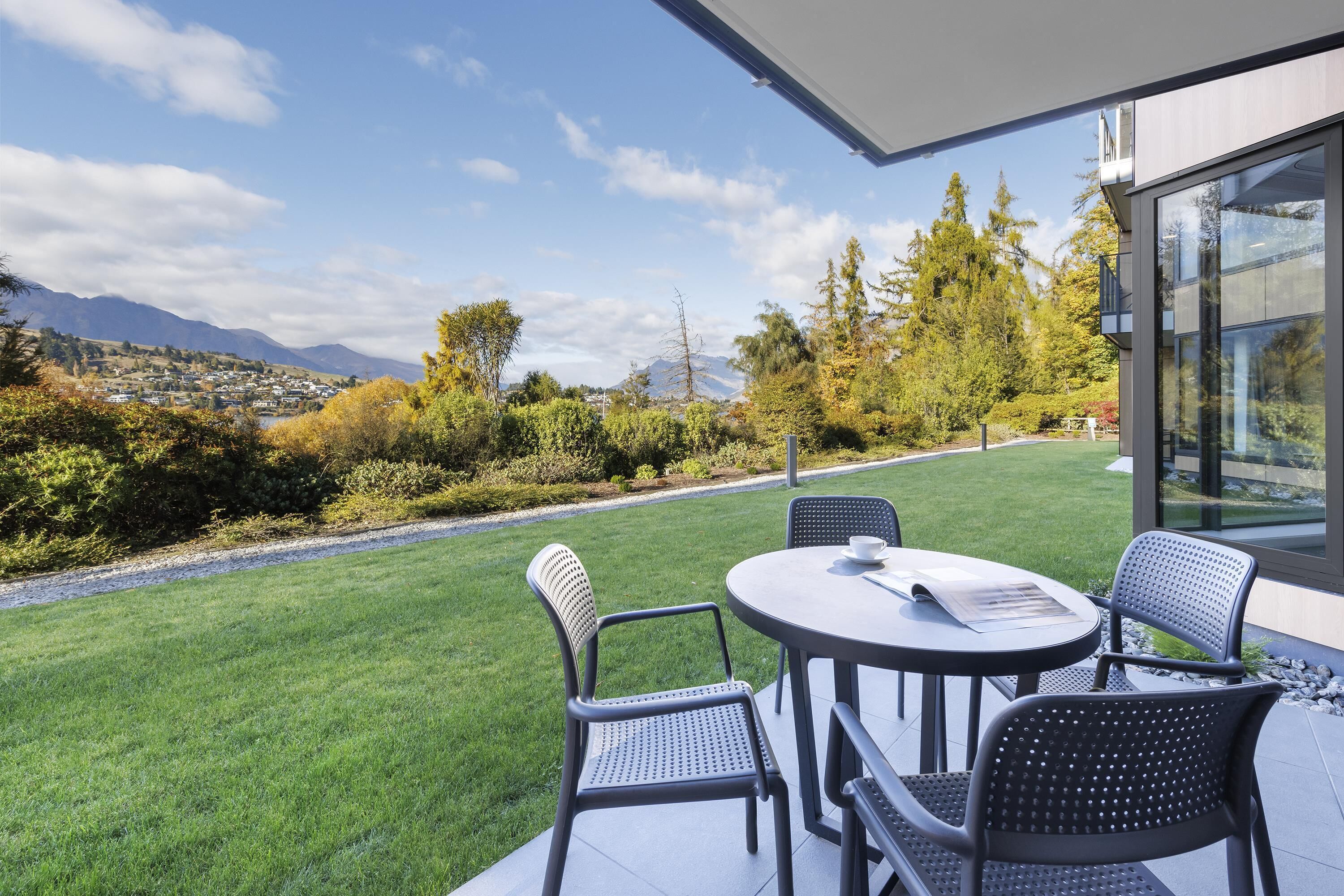 A patio with a table and chairs, overlooking a well-maintained lawn and distant mountains.