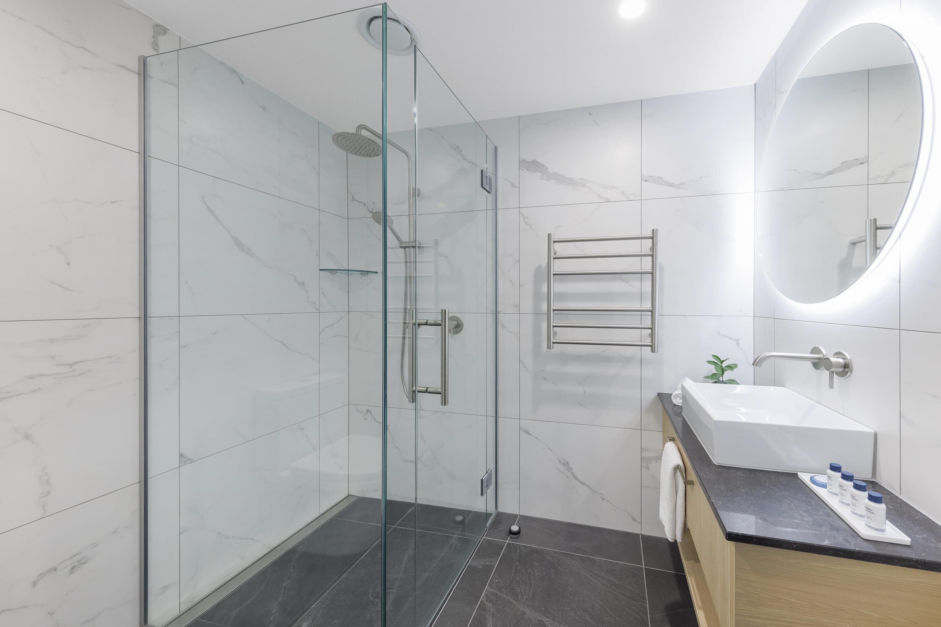 Une salle de bain moderne avec une douche à parois de verre, un grand miroir, un lavabo et un porte-serviettes.