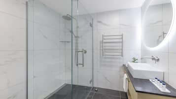 Une salle de bain moderne avec une douche à parois de verre, un grand miroir, un lavabo et un porte-serviettes.