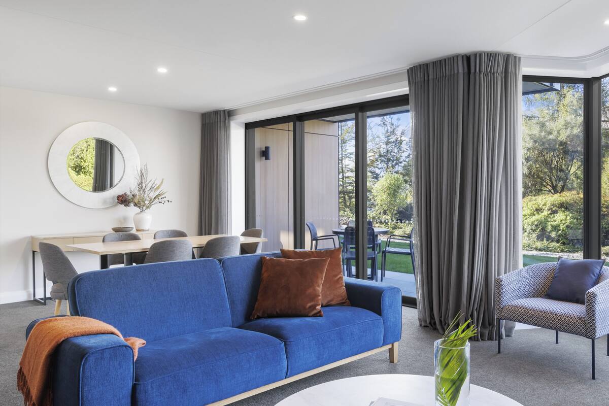 Una sala de estar moderna con un sofá azul, una mesa de centro redonda y un comedor al fondo.