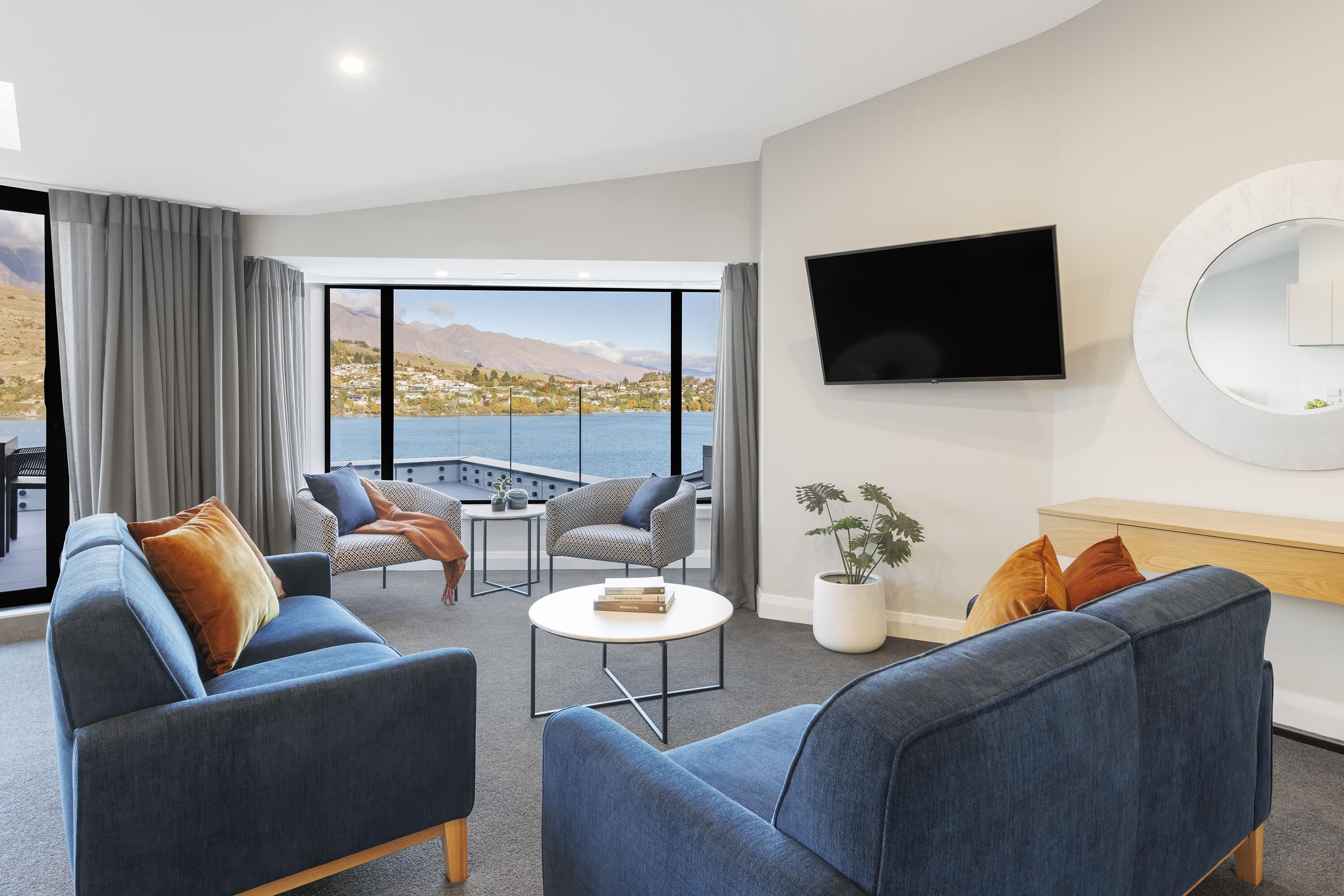 Un salon moderne avec un canapé, des fauteuils, une table basse et un téléviseur fixé au mur.