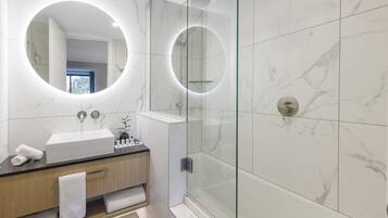 A modern bathroom with a glass-enclosed shower, a round mirror, and a white sink.