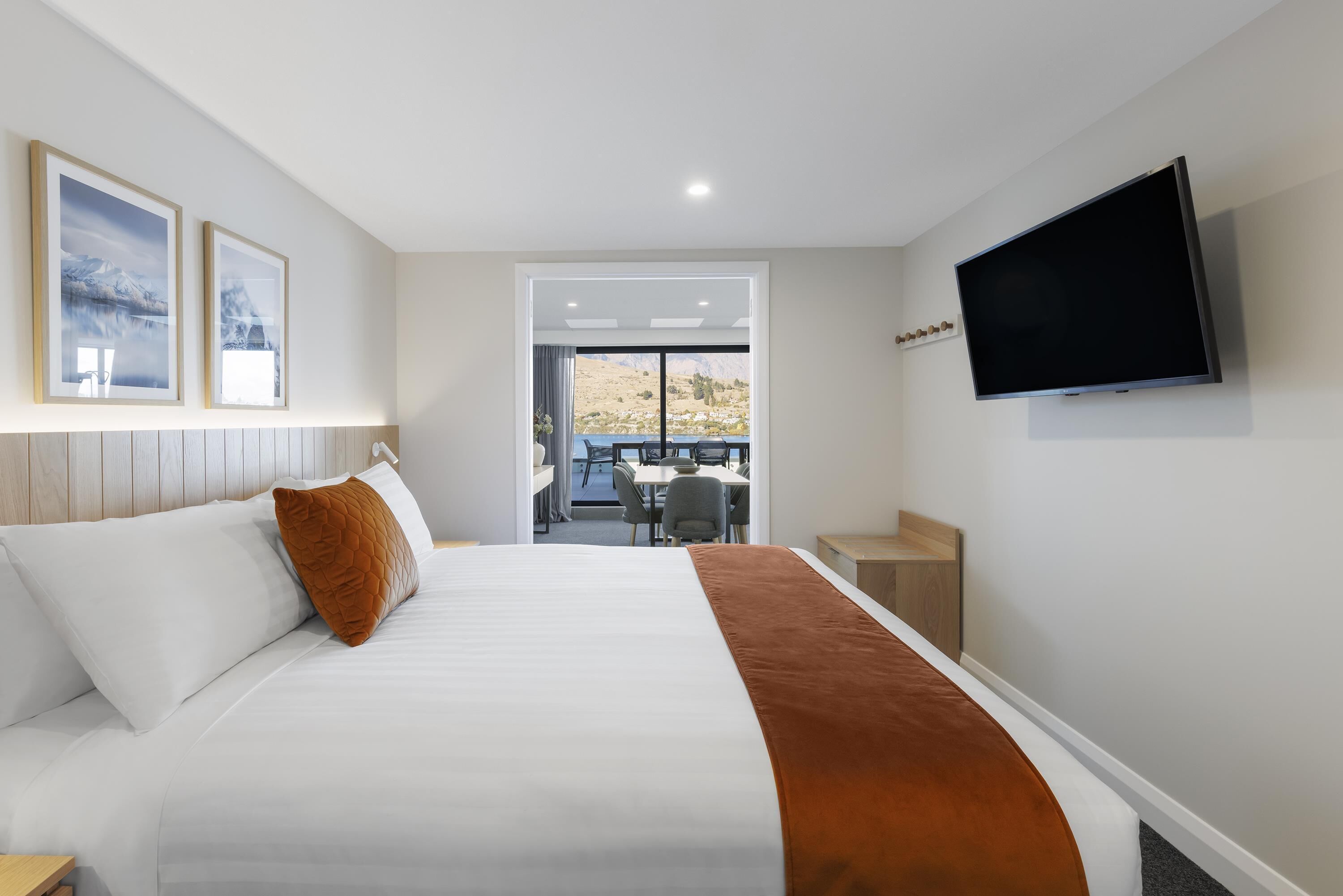 A hotel room with a bed, a TV mounted on the wall, and a view of the outdoors through a door.