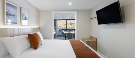 A hotel room with a bed, a TV mounted on the wall, and a view of the outdoors through a door.
