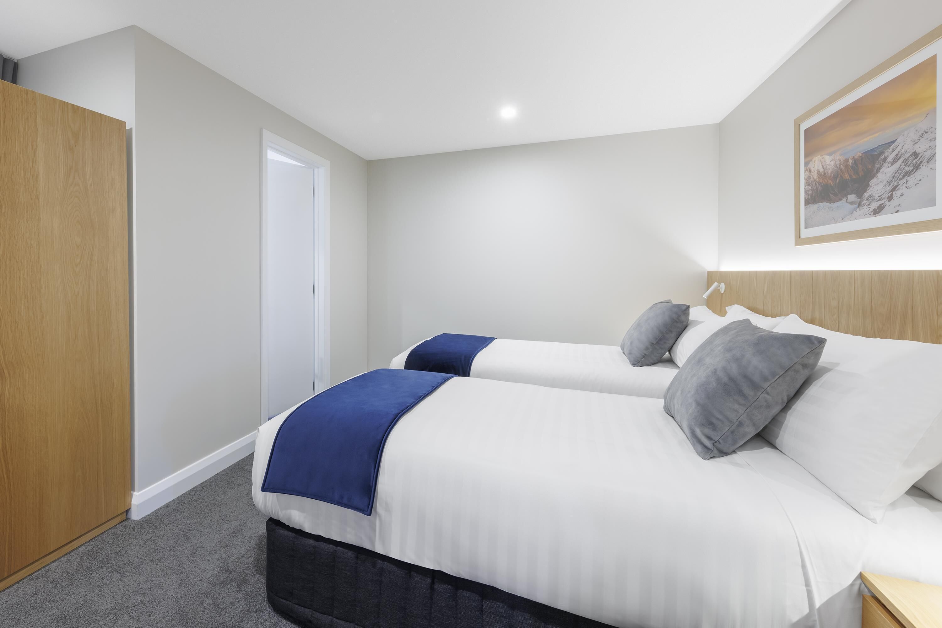 A bedroom with two beds, a wooden wardrobe, a door, and a framed picture on the wall.